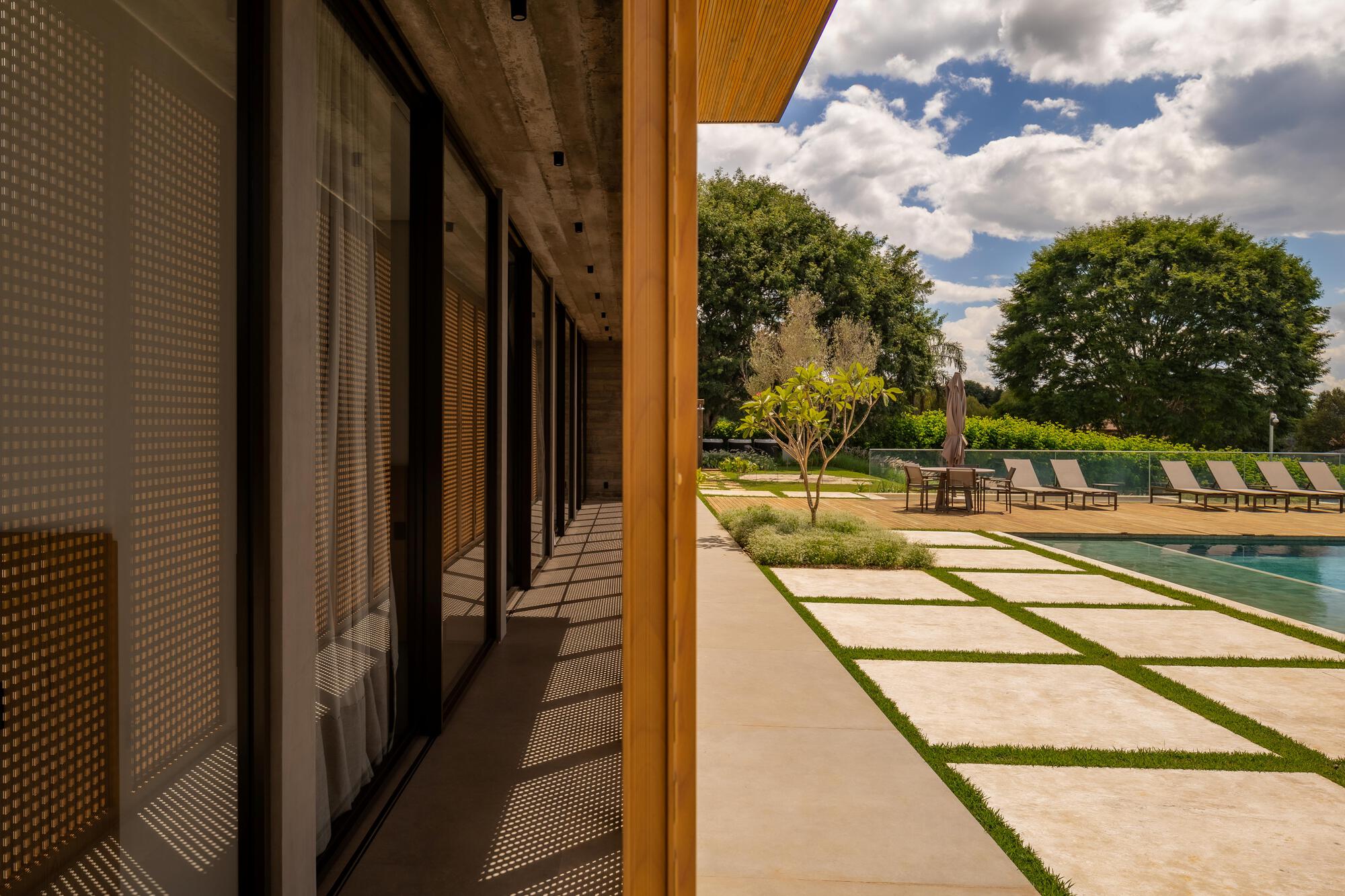 Covered walkway with perforated sliding screens along the glazed facade opening to the pool terrace