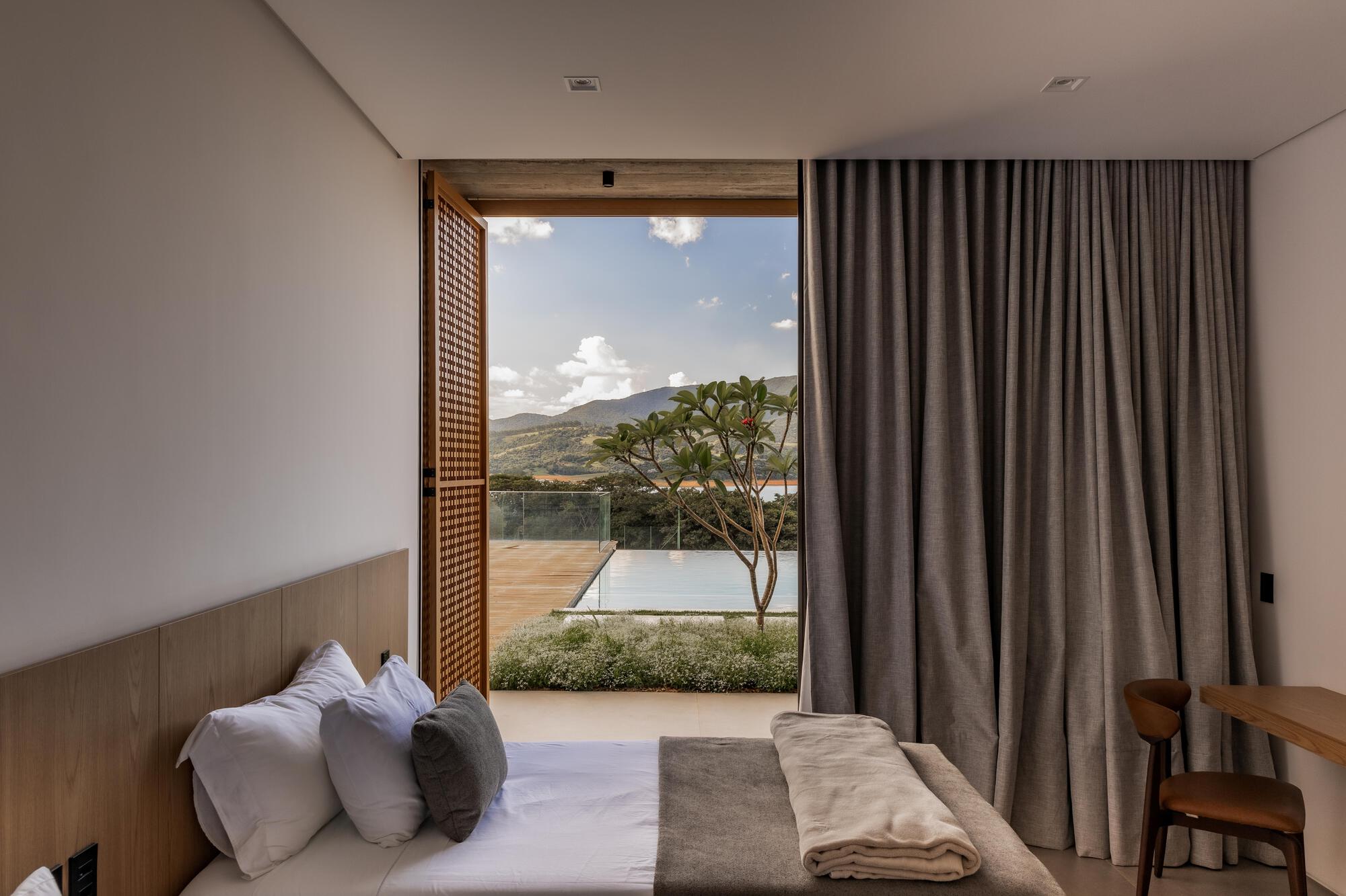 Bedroom with latticed timber sliding screen opening to terrace and pool under afternoon clouds