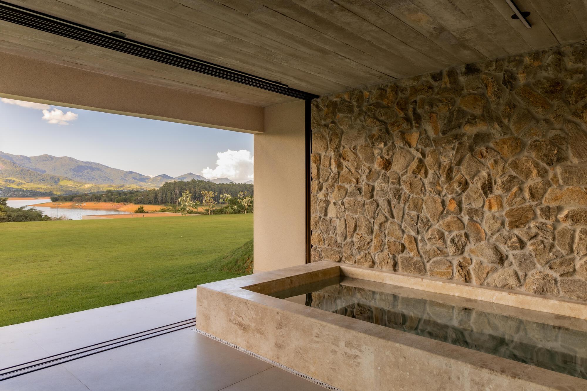 Travertine bathtub against irregular stone wall framing views of farmland and distant mountains