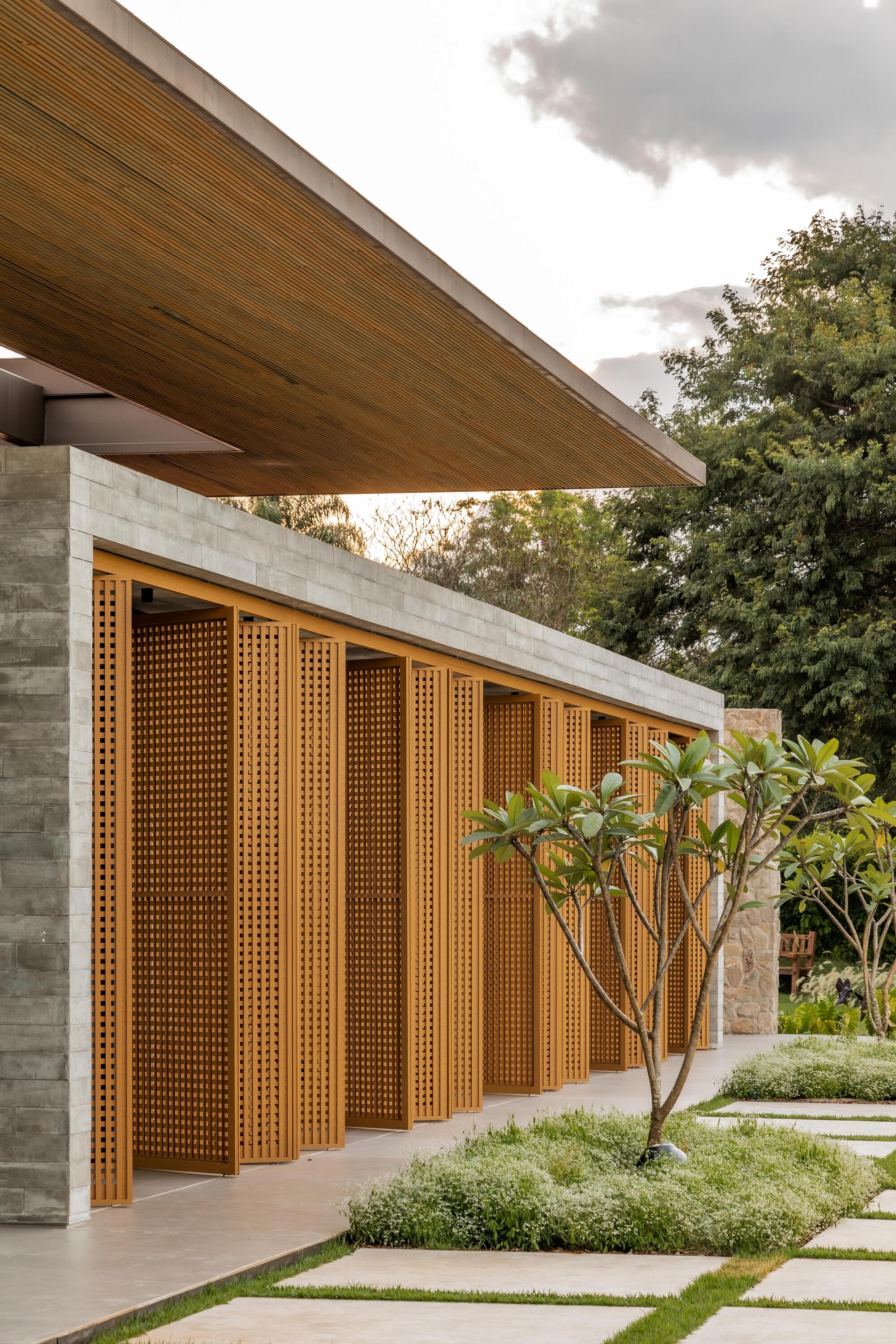 Perforated timber facade panels between concrete piers and planted beds with frangipani trees