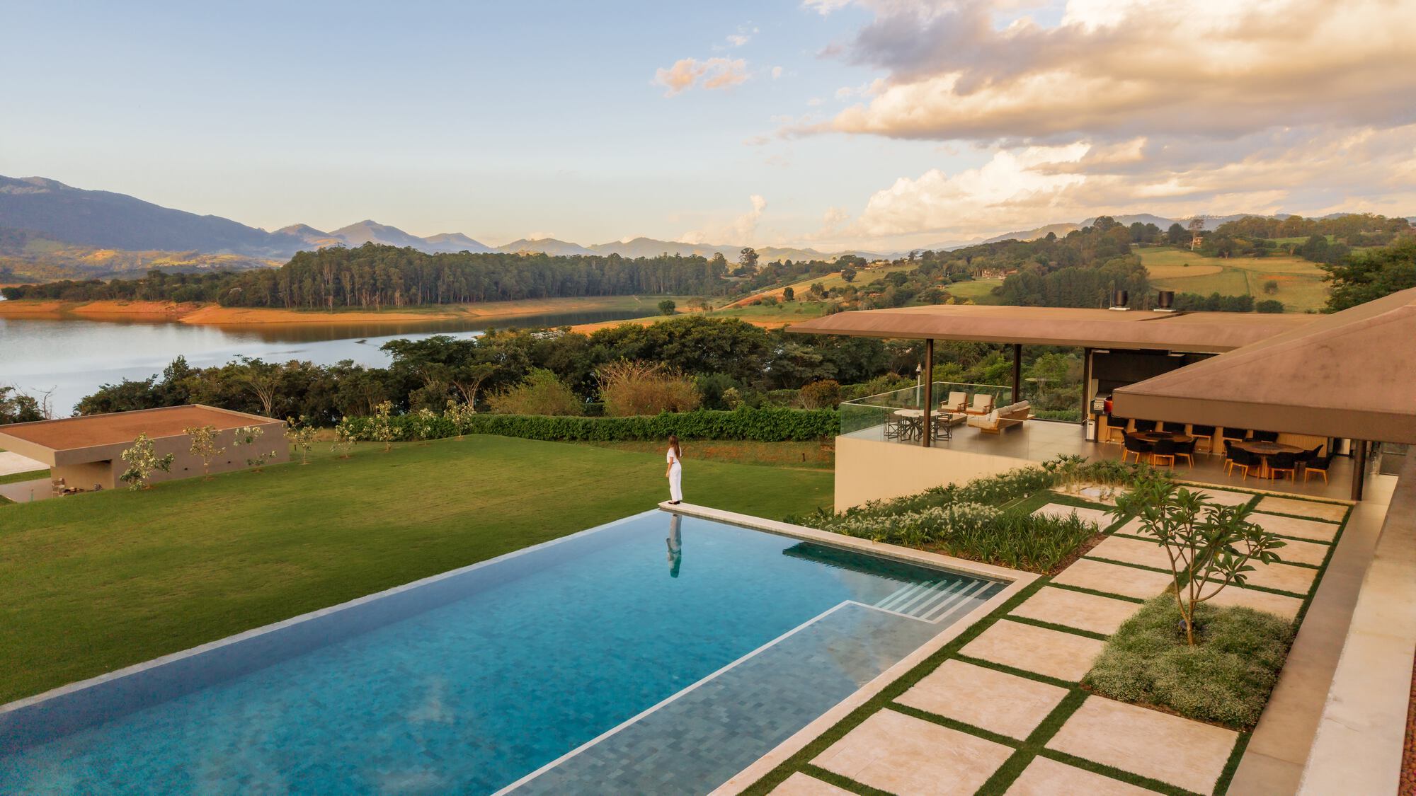 Infinity pool at dusk overlooking reservoir and rolling hills with covered terrace beyond