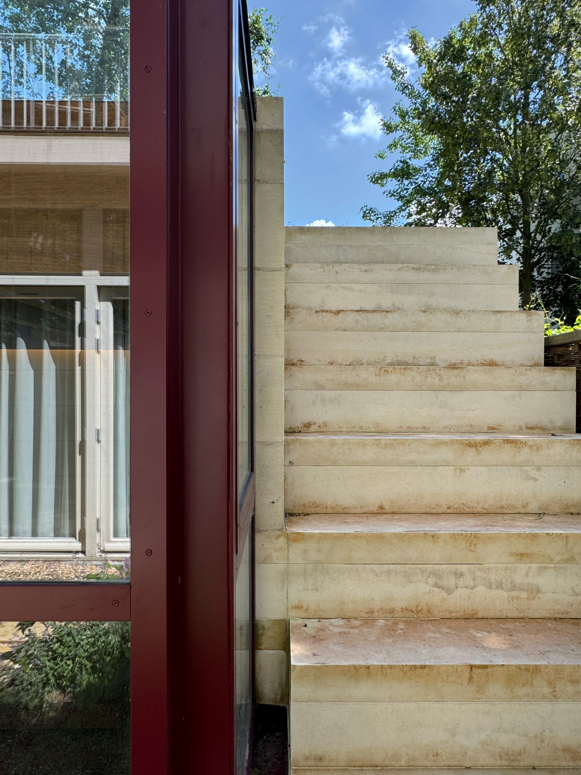 Detail of the red steel window frame meeting the poured concrete staircase under a bright sky