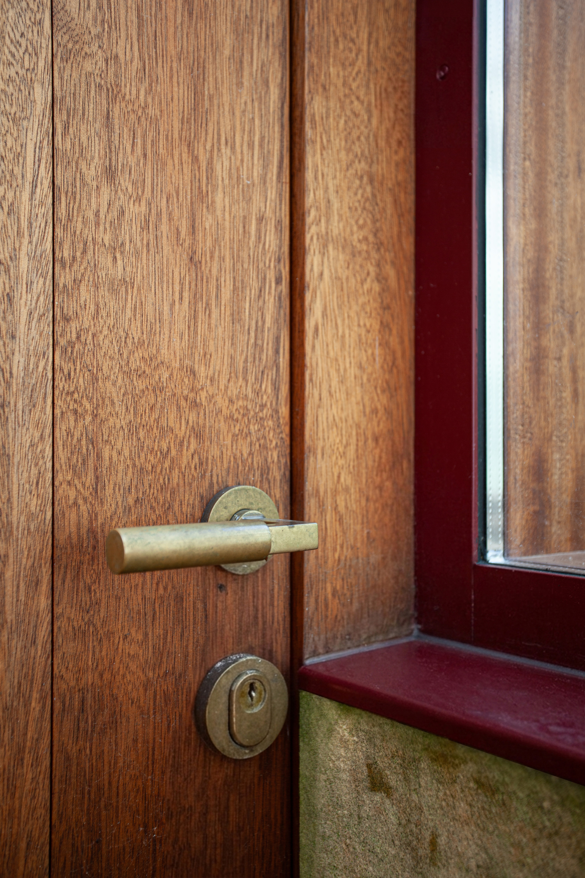 Close-up of brass door handle and lock cylinder on timber door next to red steel frame