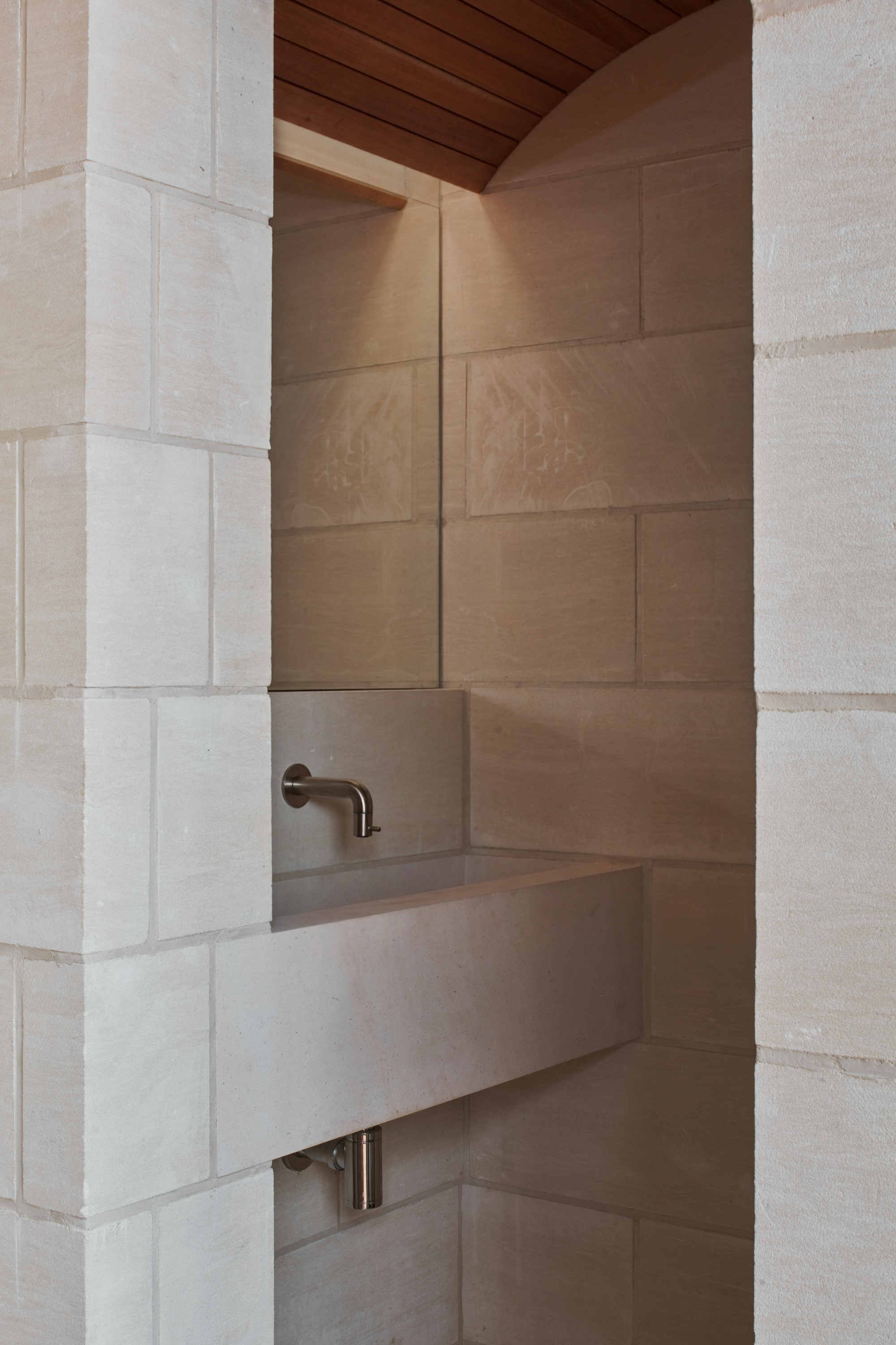 Limestone basin wall with bronze tap fixture beneath a timber ceiling soffit