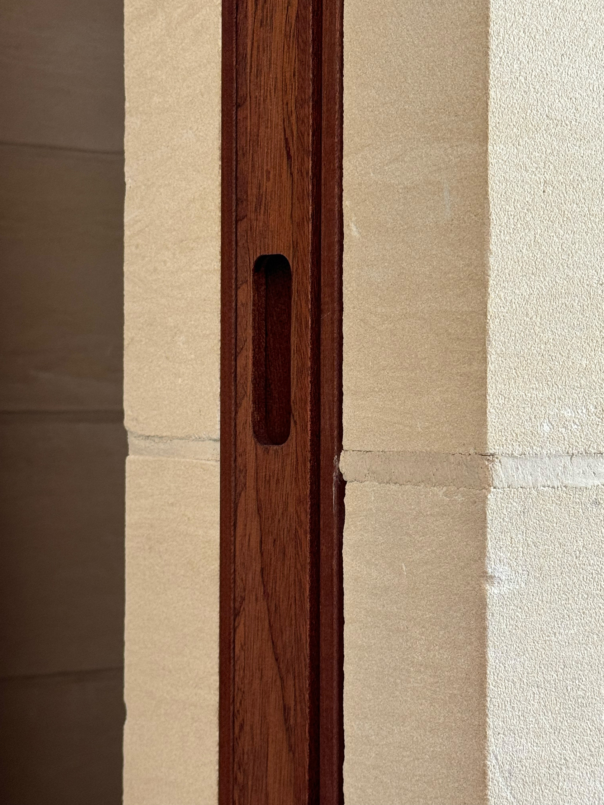 Detail of timber door pull recessed into the darkwood frame against a limestone wall in afternoon sunlight