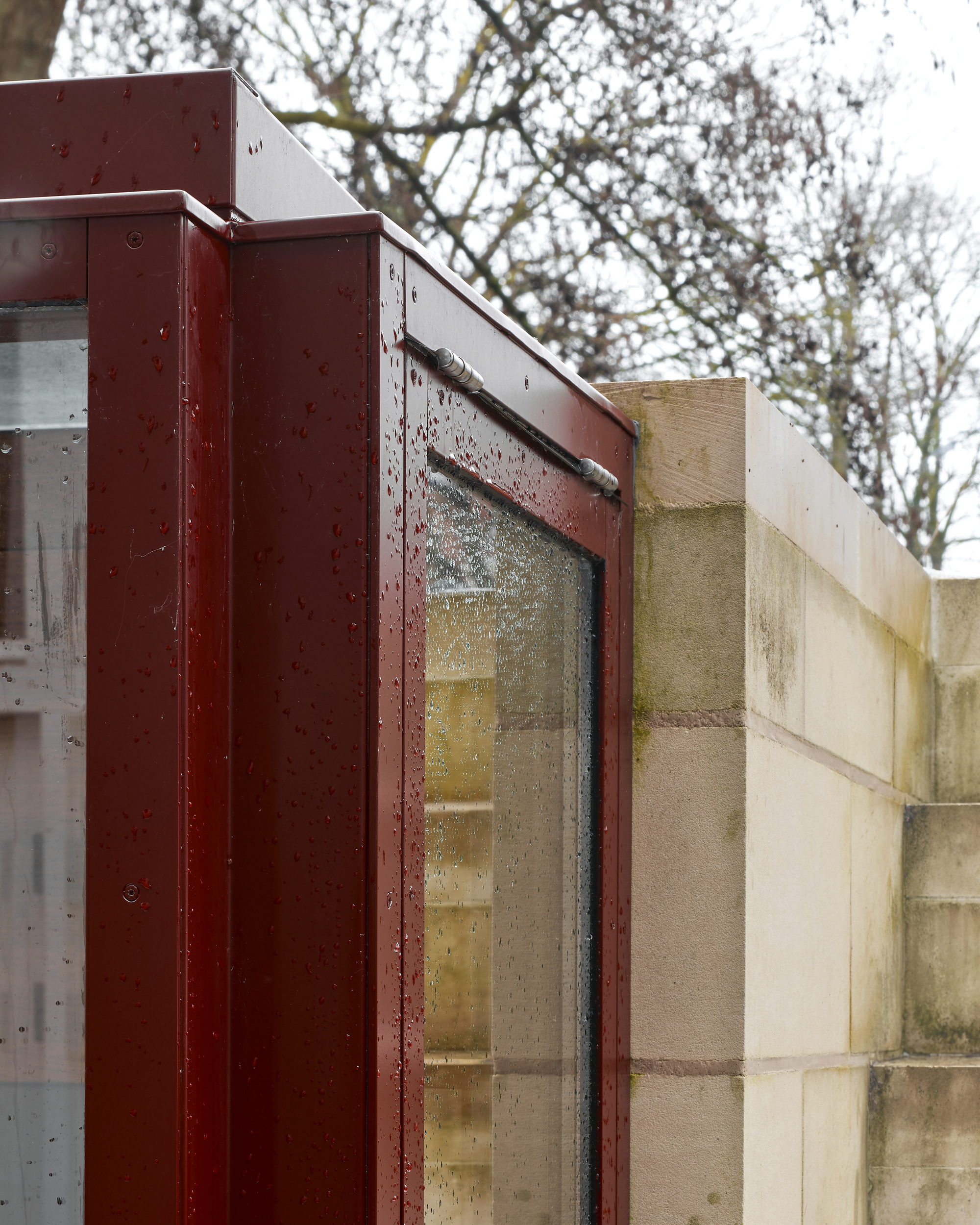 Rainspattered steel window frame meeting limestone block wall beneath bare winter tree branches