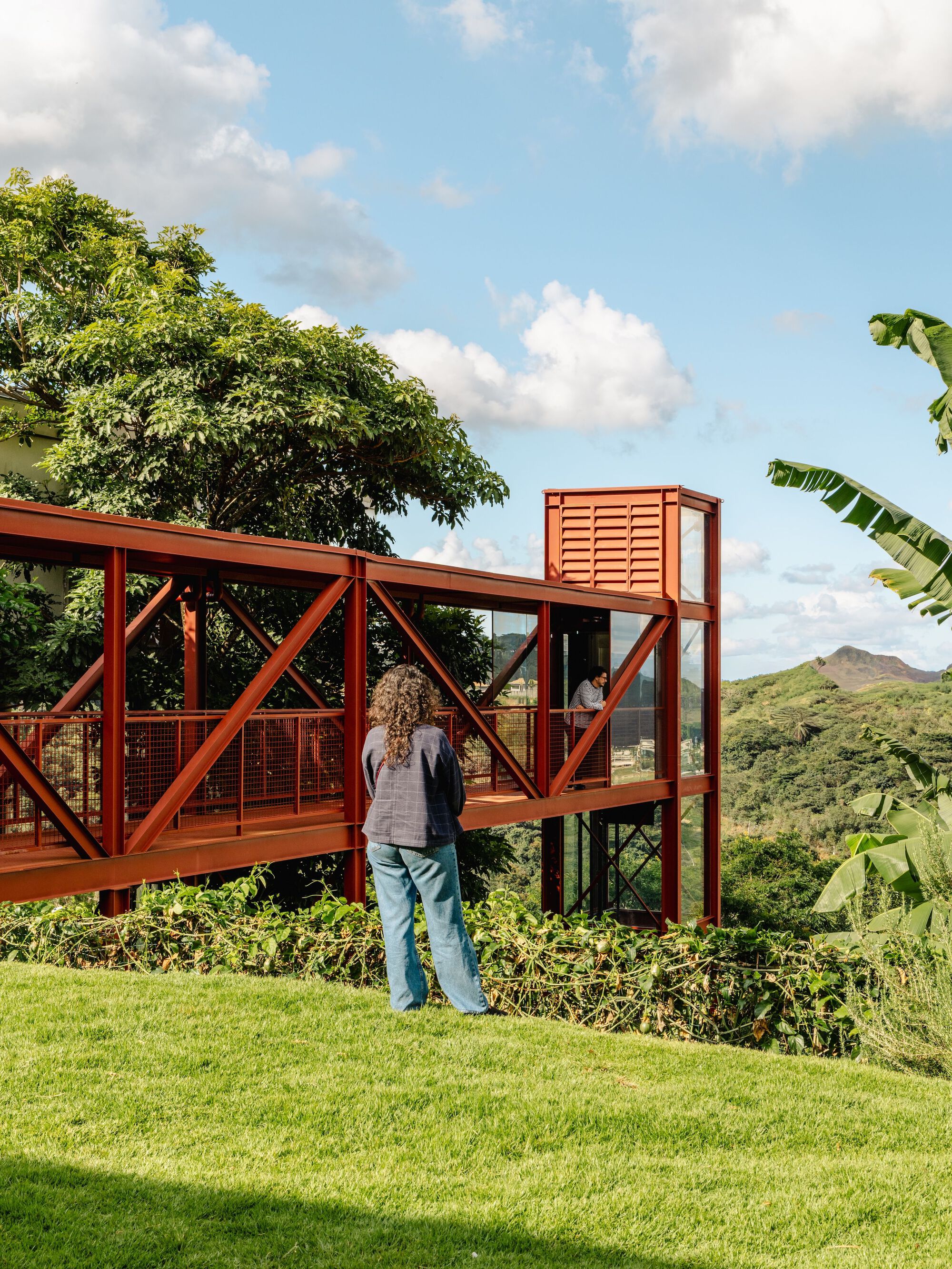 Elevated steel frame walkway cantilevering over the hillside with a person looking toward distant hills