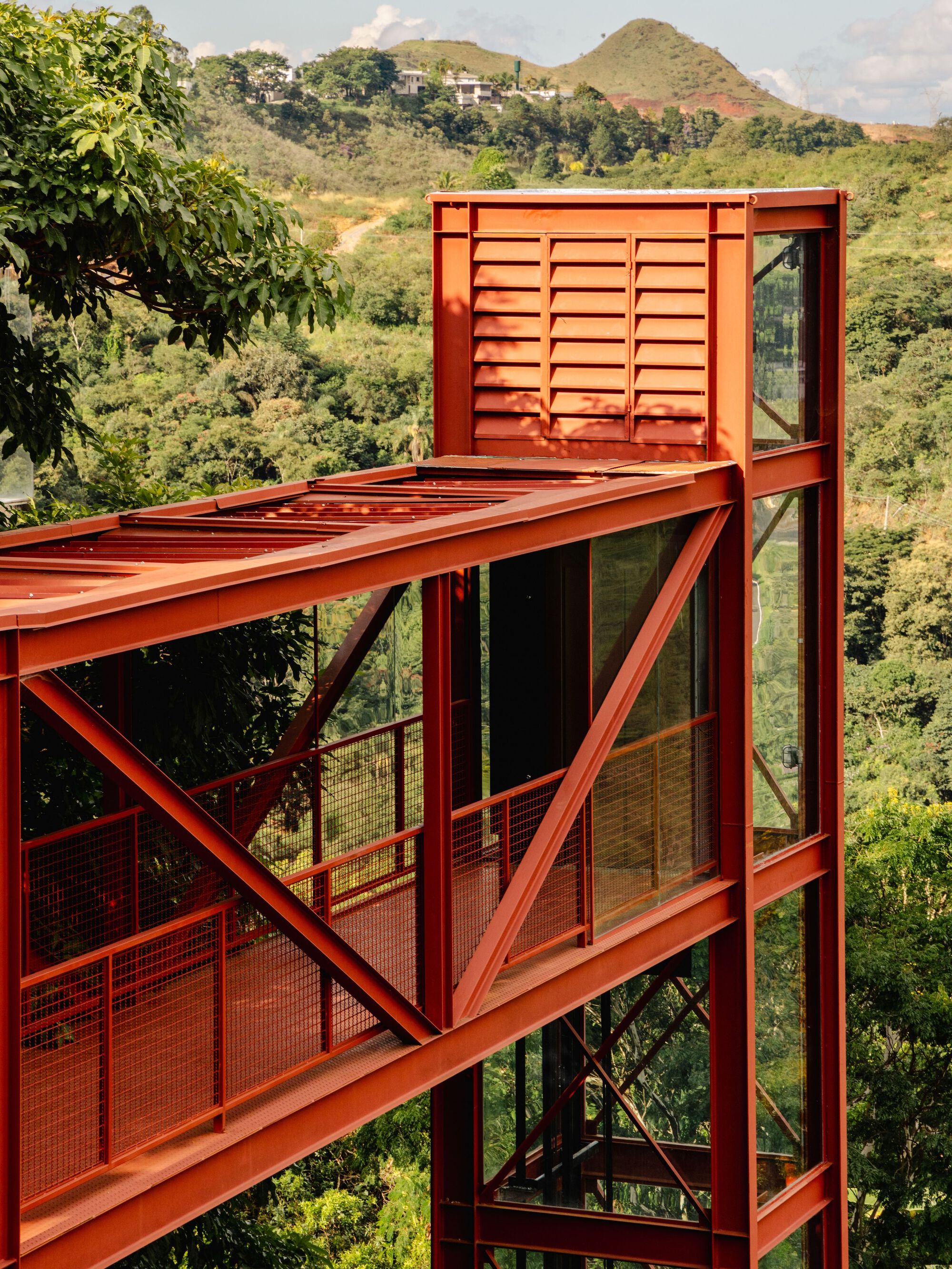 Red steel structural frame with diagonal bracing and louvered mechanical enclosure overlooking the valley below