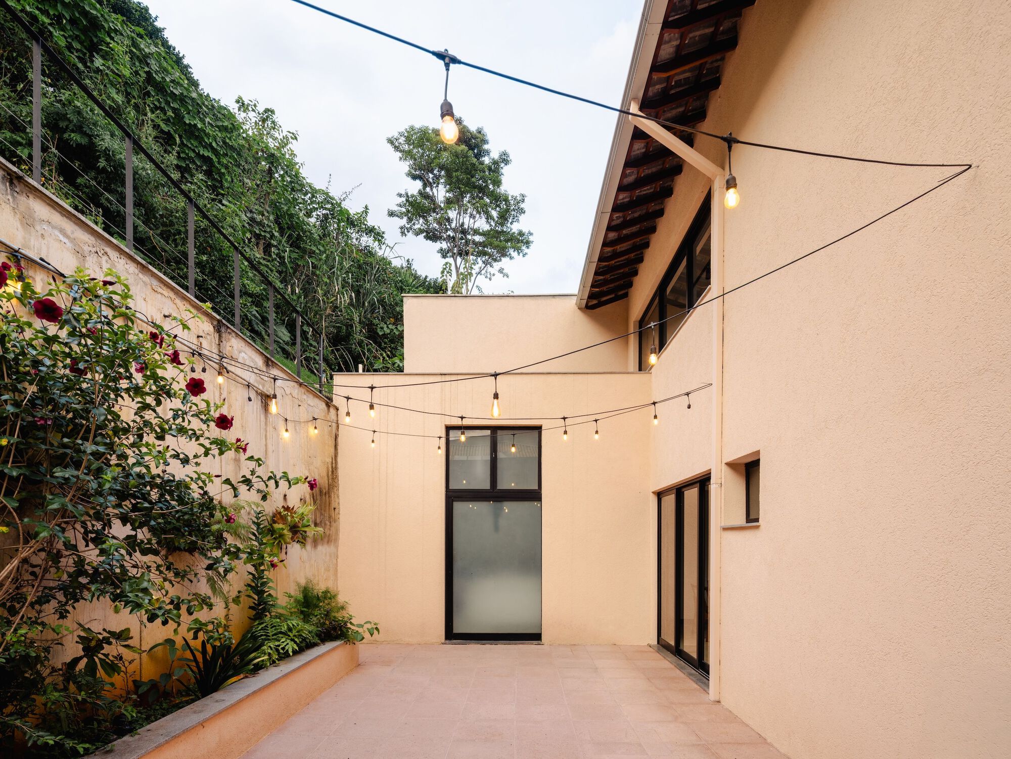 Exterior courtyard with string lights overhead and concrete retaining wall covered in climbing vines at dusk