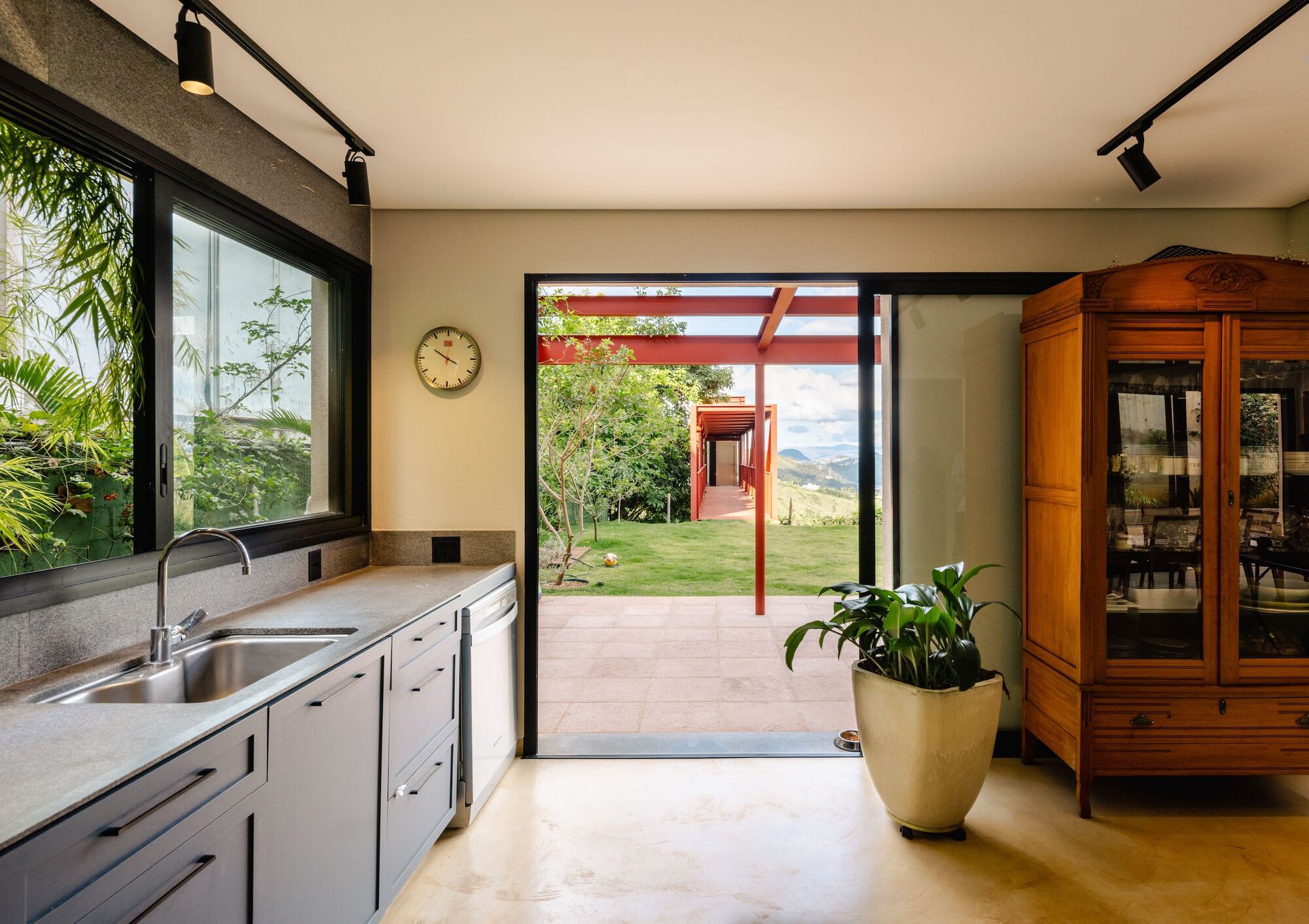 Kitchen view through open sliding door to exterior porch with red steel frame and hillside beyond