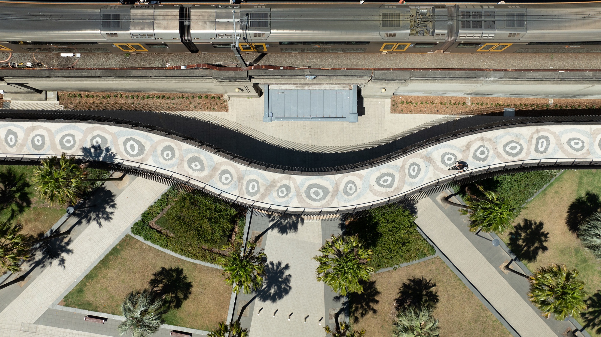 Aerial view of the curving pedestrian pathway with circular paver patterns alongside planted beds and palm trees