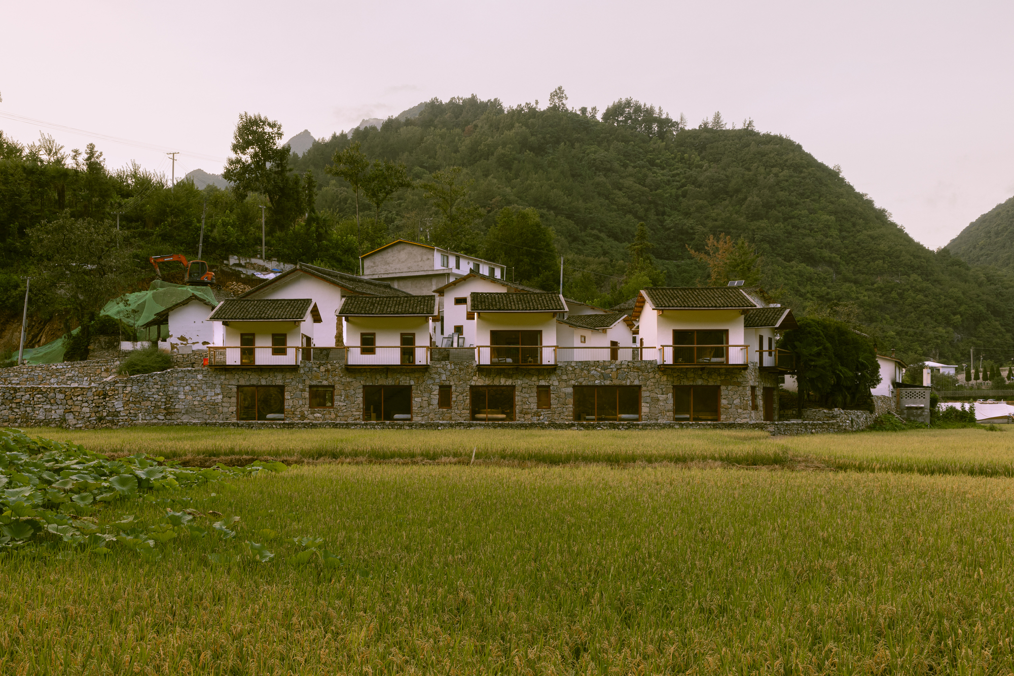 Front elevation showing repeated gable volumes above a continuous stone retaining wall at dusk