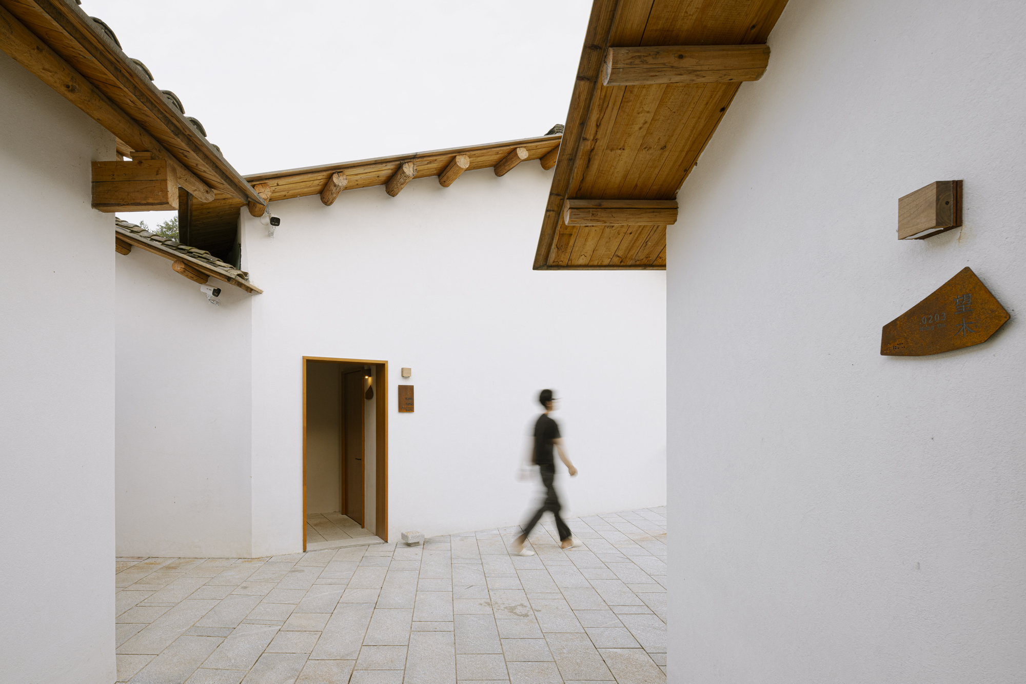 Open courtyard with white walls and exposed timber eaves as a figure walks across stone pavers