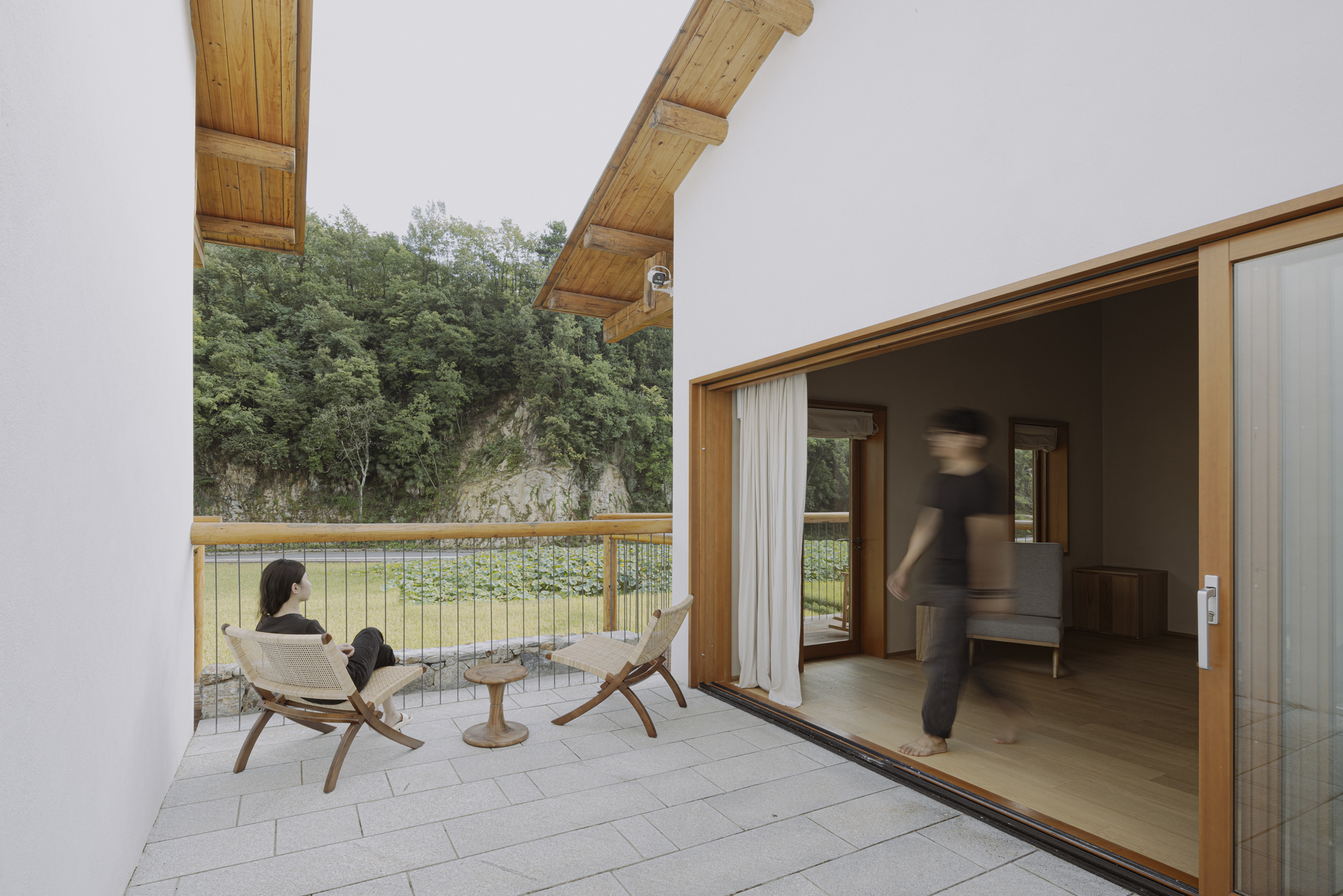 Covered terrace opening to interior living space with figures seated outside and moving through the doorway