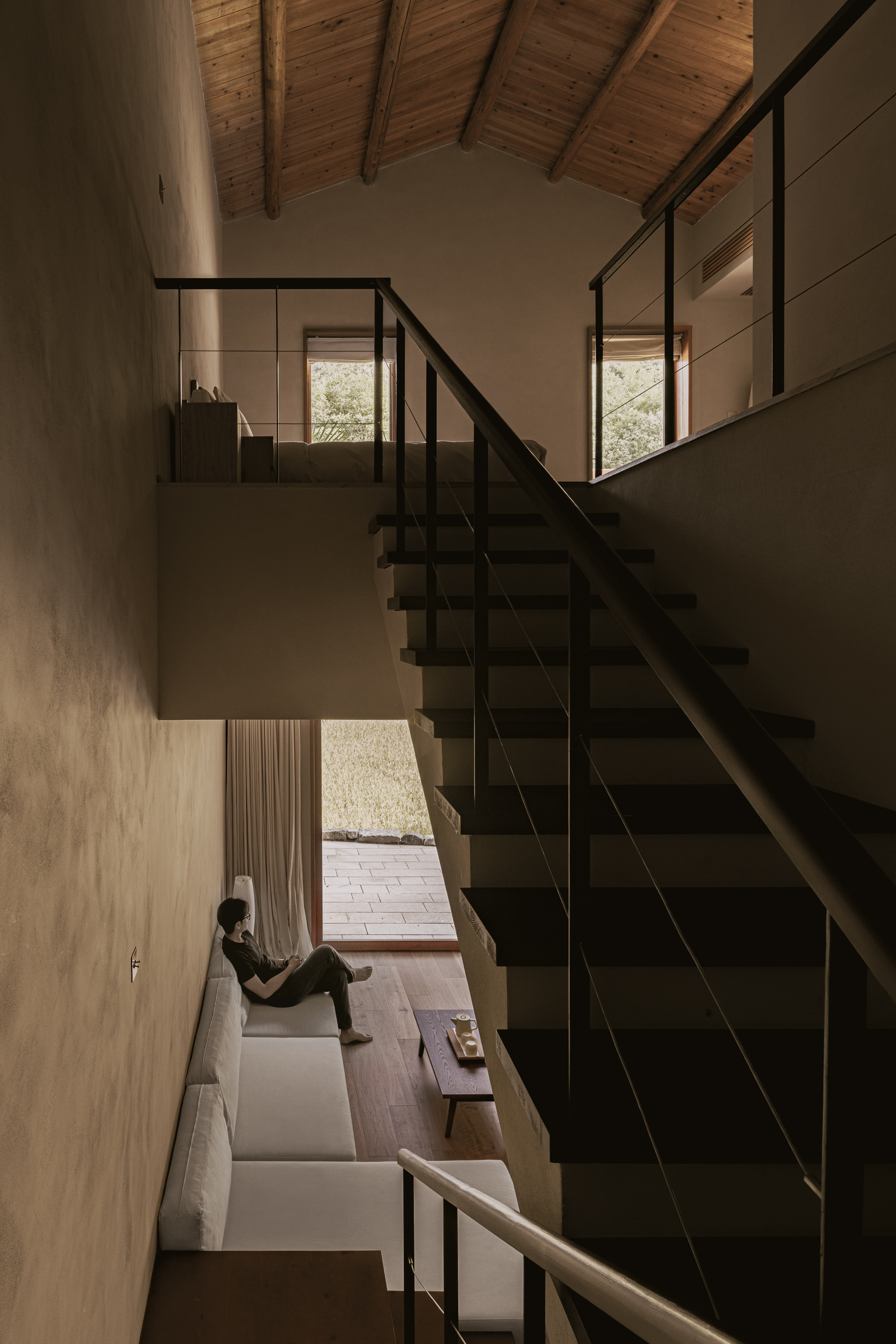 Double-height space with black steel stair and person seated by window below