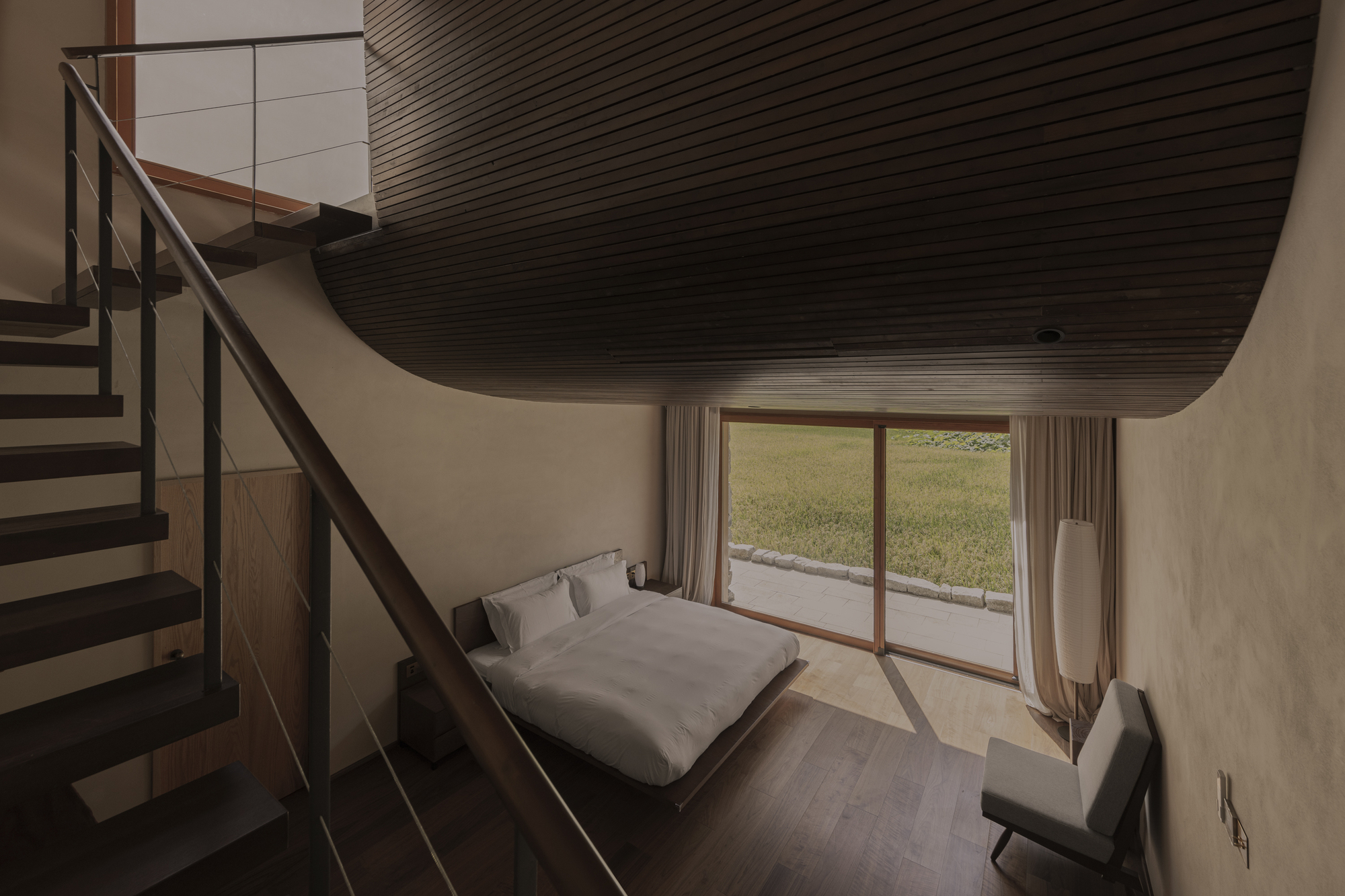 Bedroom with curved timber slat ceiling, steel staircase and glass door opening to a grassy courtyard