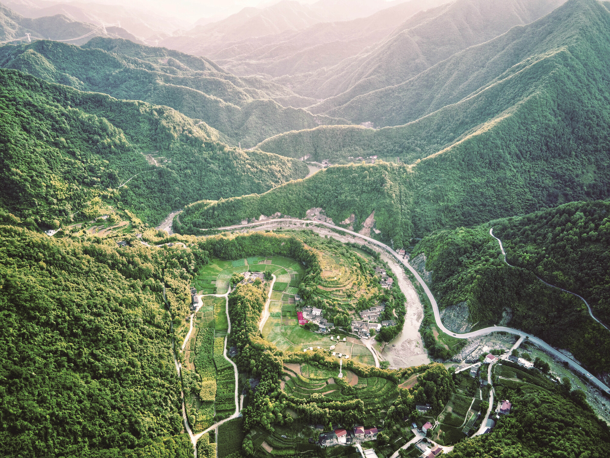 Aerial view of terraced agricultural fields and a small cluster of structures in a forested mountain valley