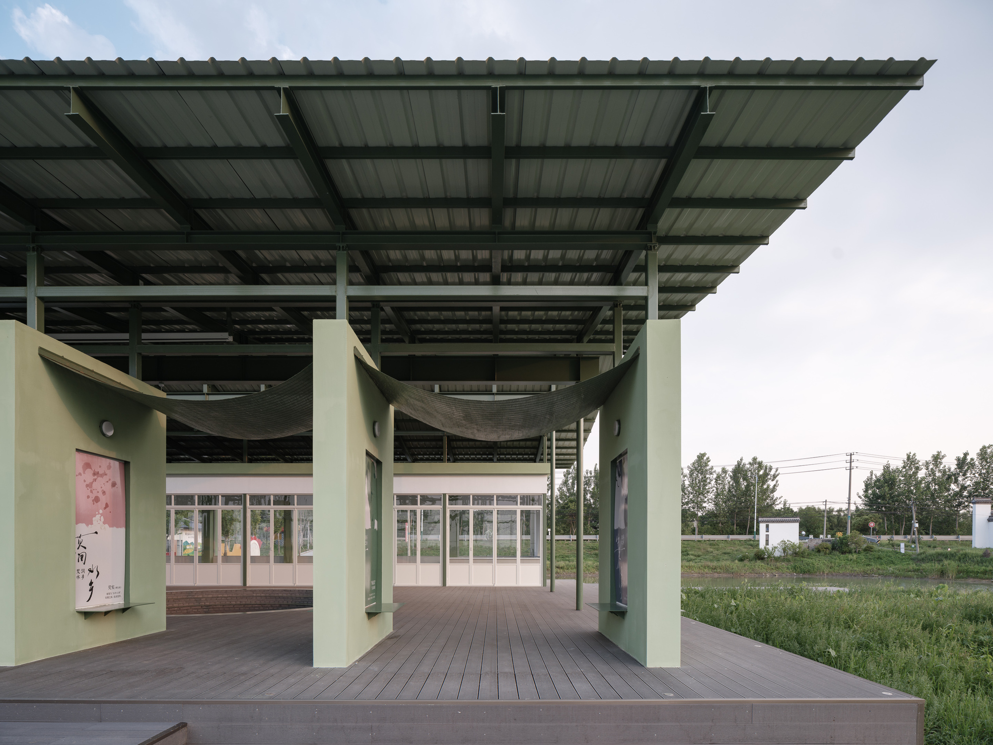 View through the covered timber deck toward the glazed entrance flanked by green walls with display panels