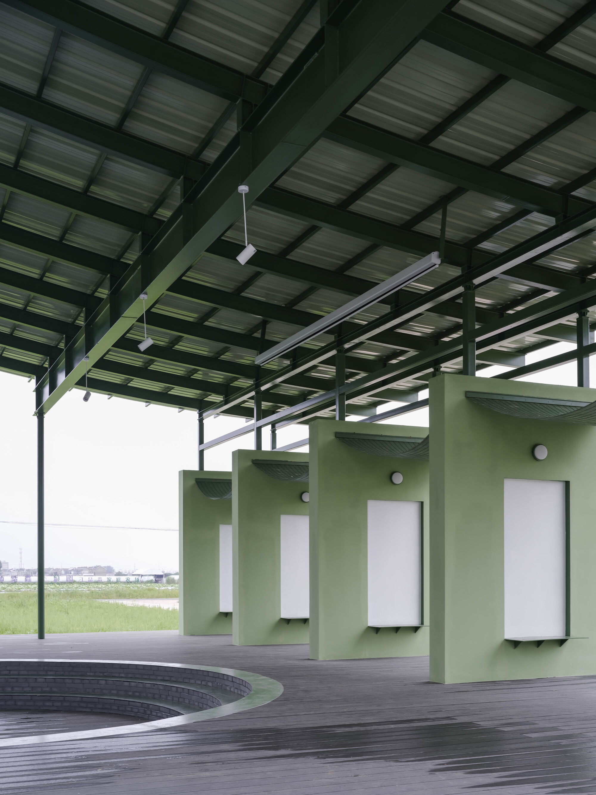 Interior view of the structural steel frame with green columns supporting the corrugated roof above exhibition panels