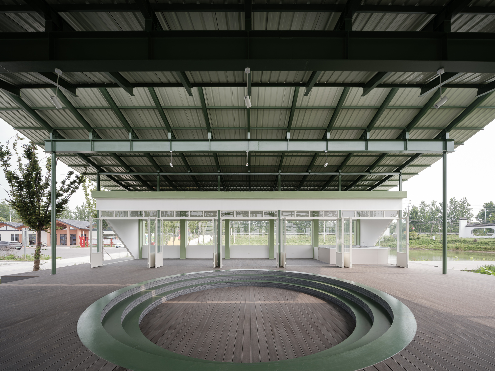 Sunken circular amphitheater beneath the open pavilion structure facing the glass-walled classroom block