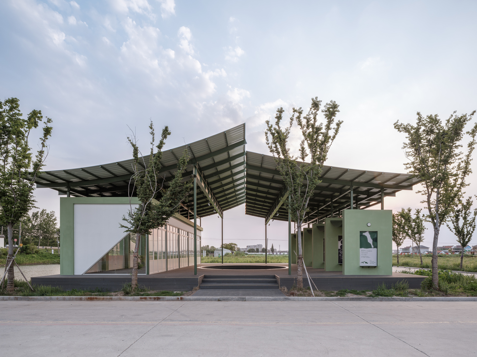 Street view showing the lifted roof canopy with young trees planted along the approach path