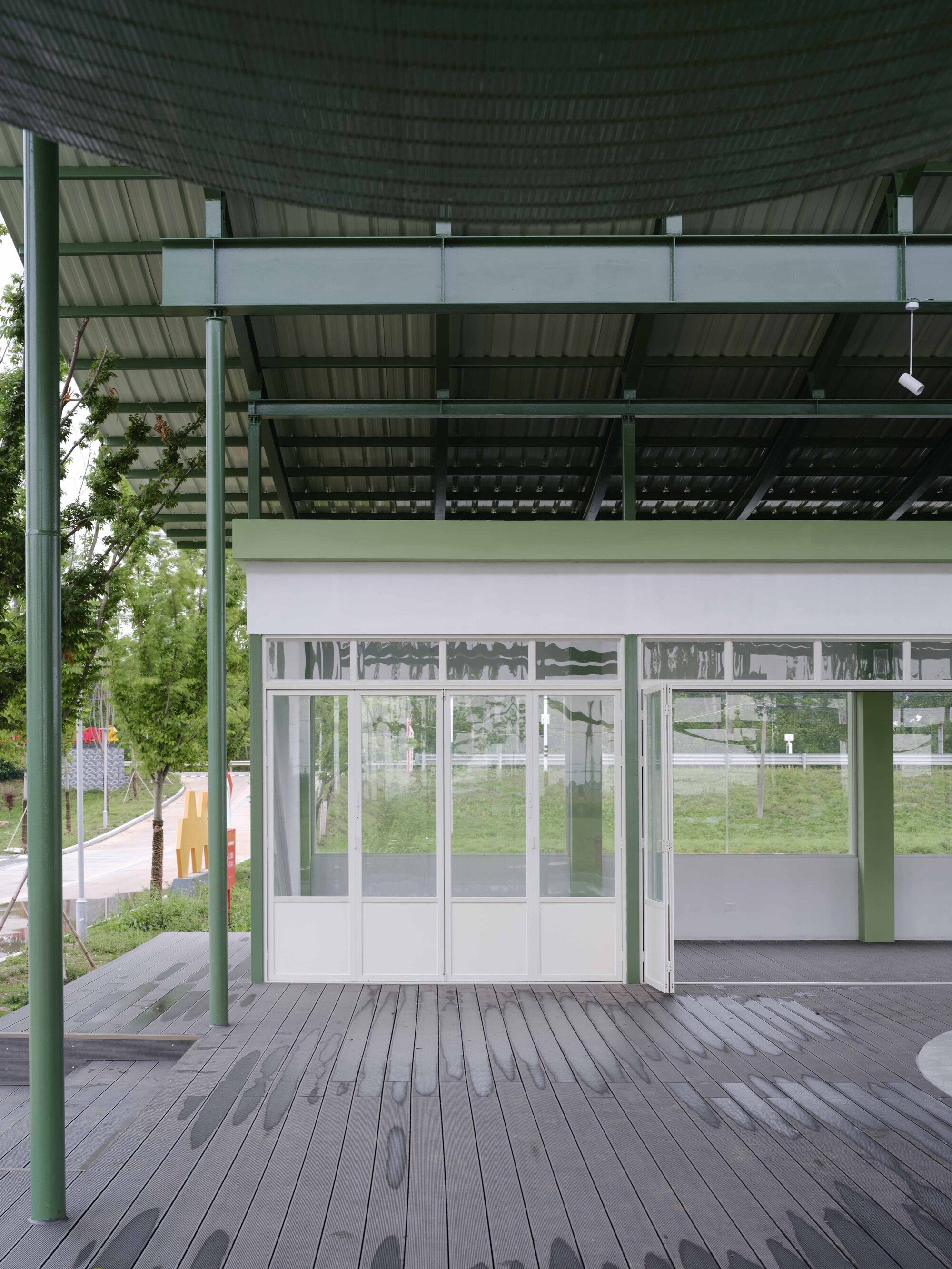 Covered deck with green steel columns and corrugated metal canopy shading glazed doors in summer