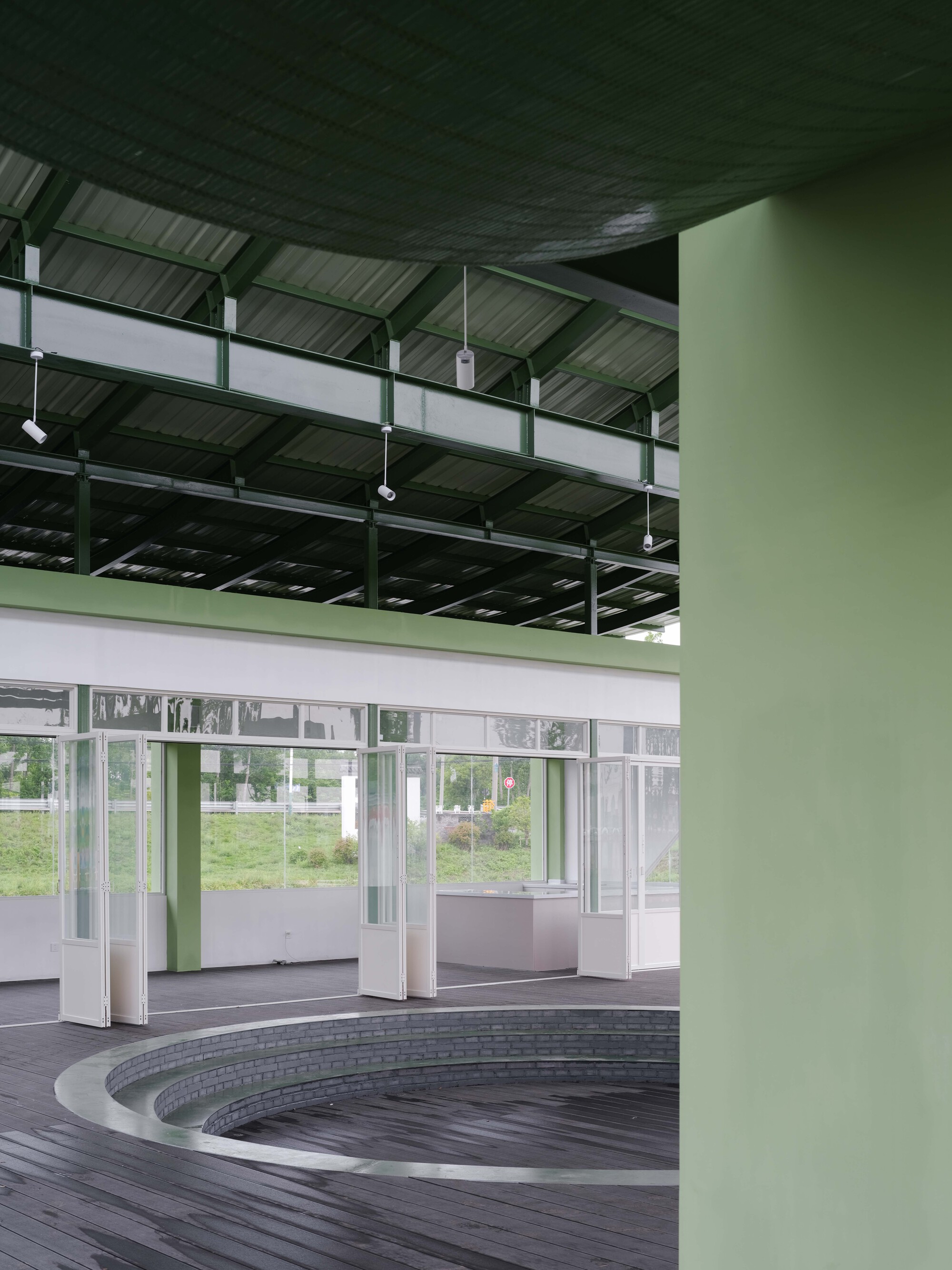 Interior space with circular timber deck around a recessed pool under exposed steel structure