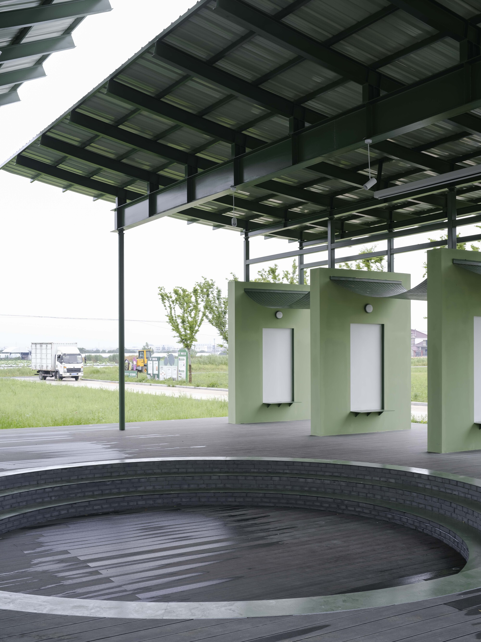 Circular timber deck with green cylindrical kiosks beneath layered solar panel canopy in daylight