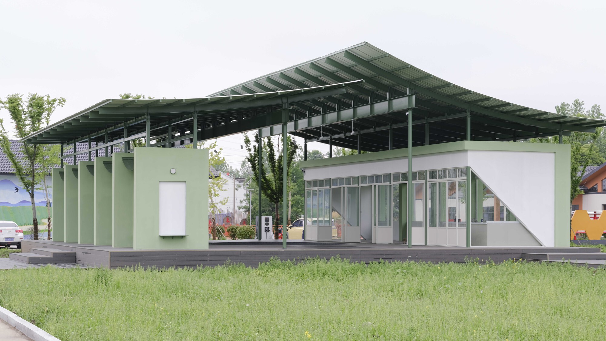 Side view of the pavilion with corrugated metal canopy above pale green paneled walls and glazed volume