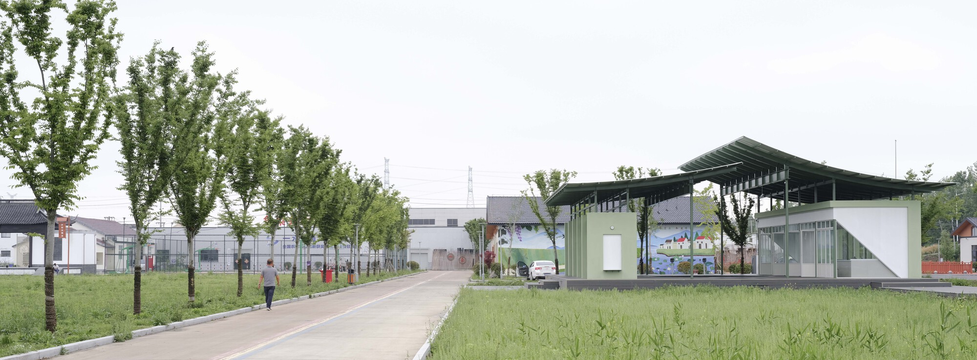 Long view along the tree-lined pathway with the canopied structure set within grassy landscape