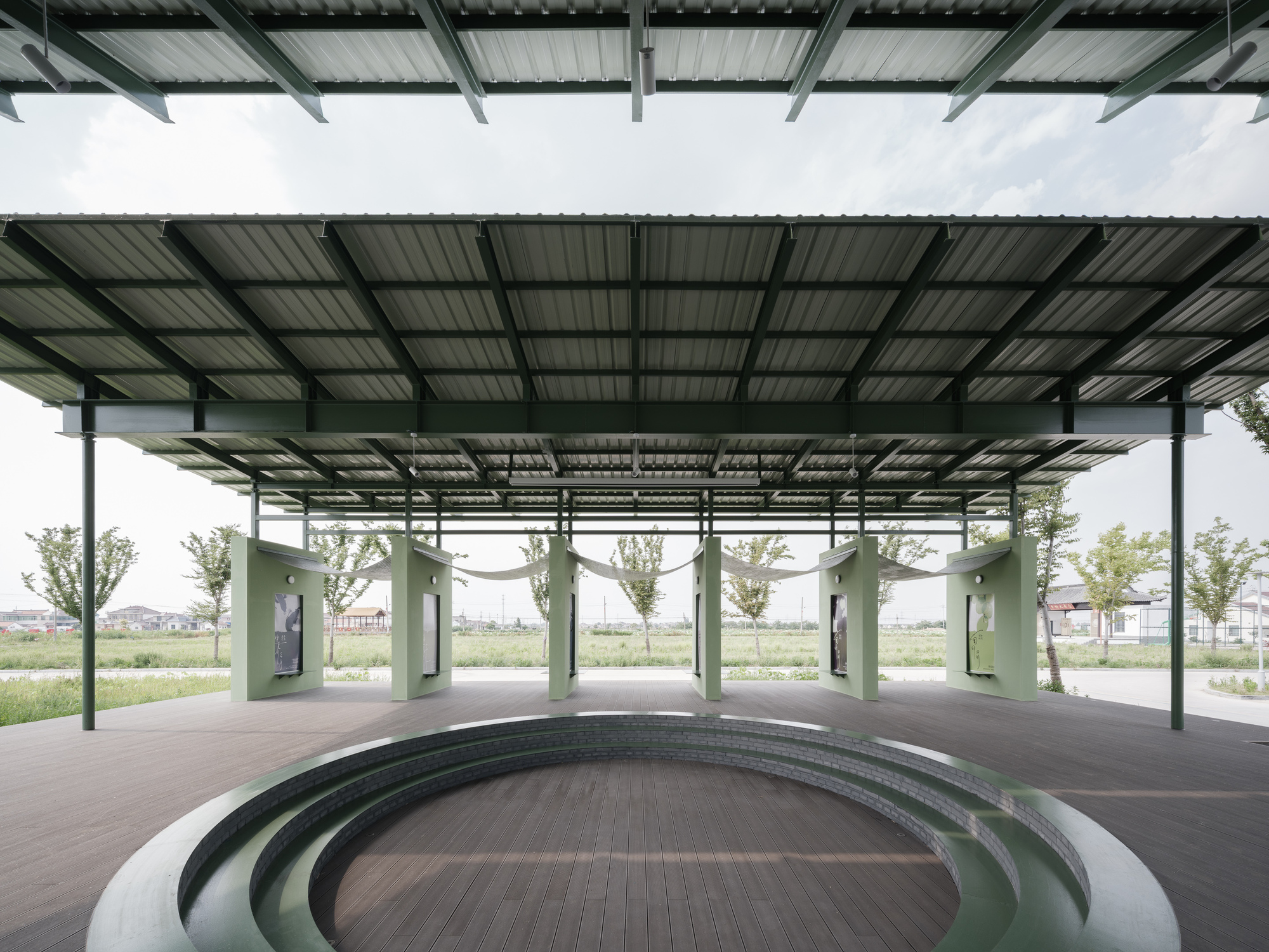 Covered outdoor gathering space with steel columns, corrugated roof and tiered circular seating platform