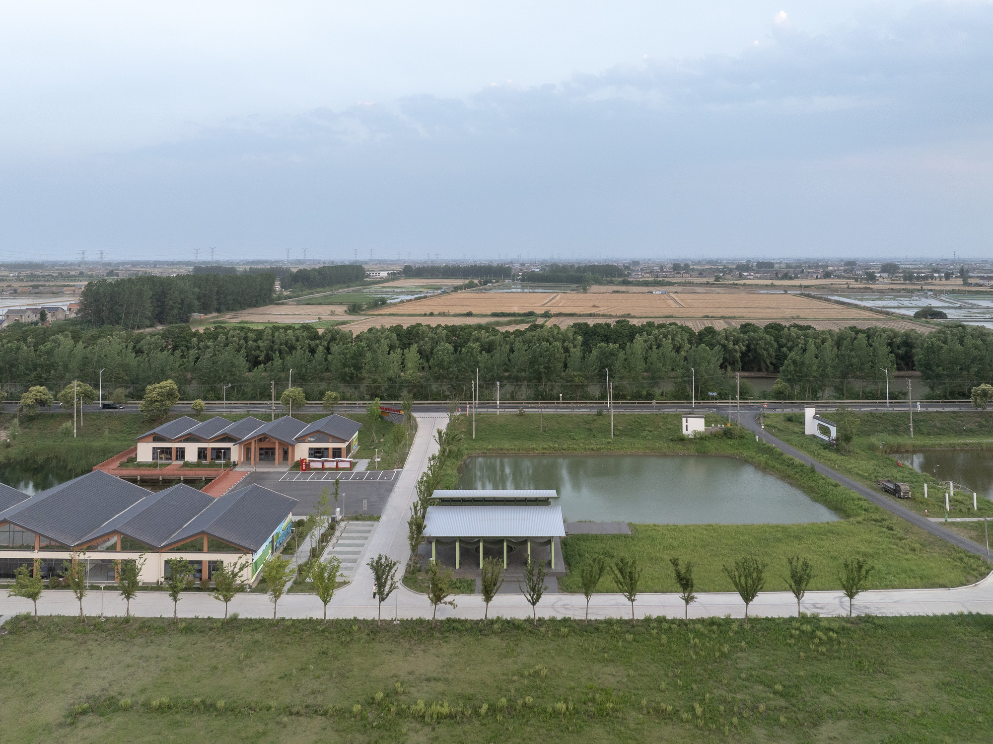 Aerial view of the site showing pavilion structures beside pond within agricultural landscape at dusk