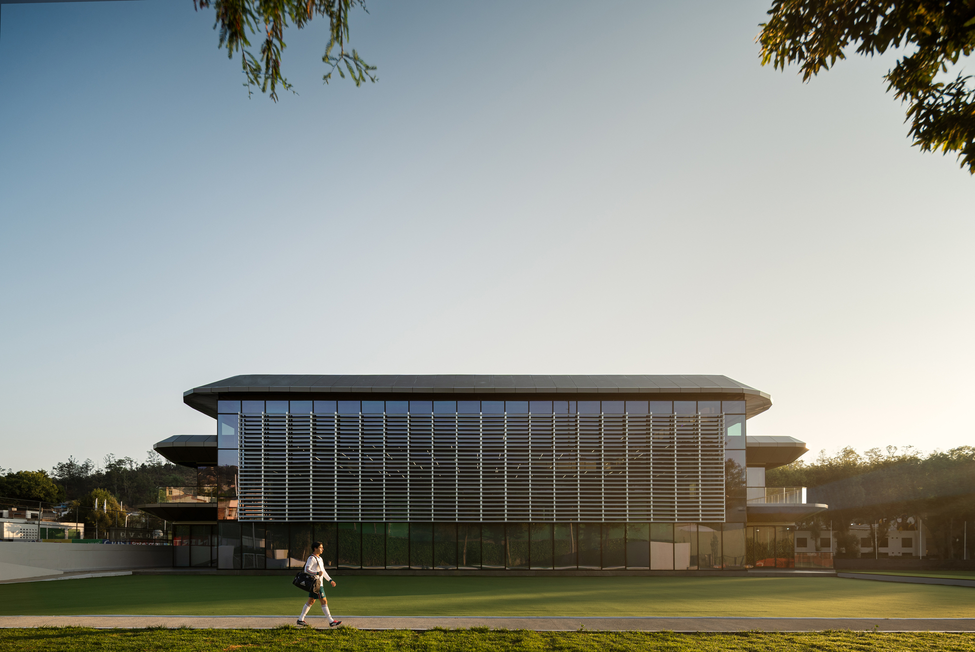 Horizontal louvered metal screen facade wrapping the upper level with a figure walking on the field