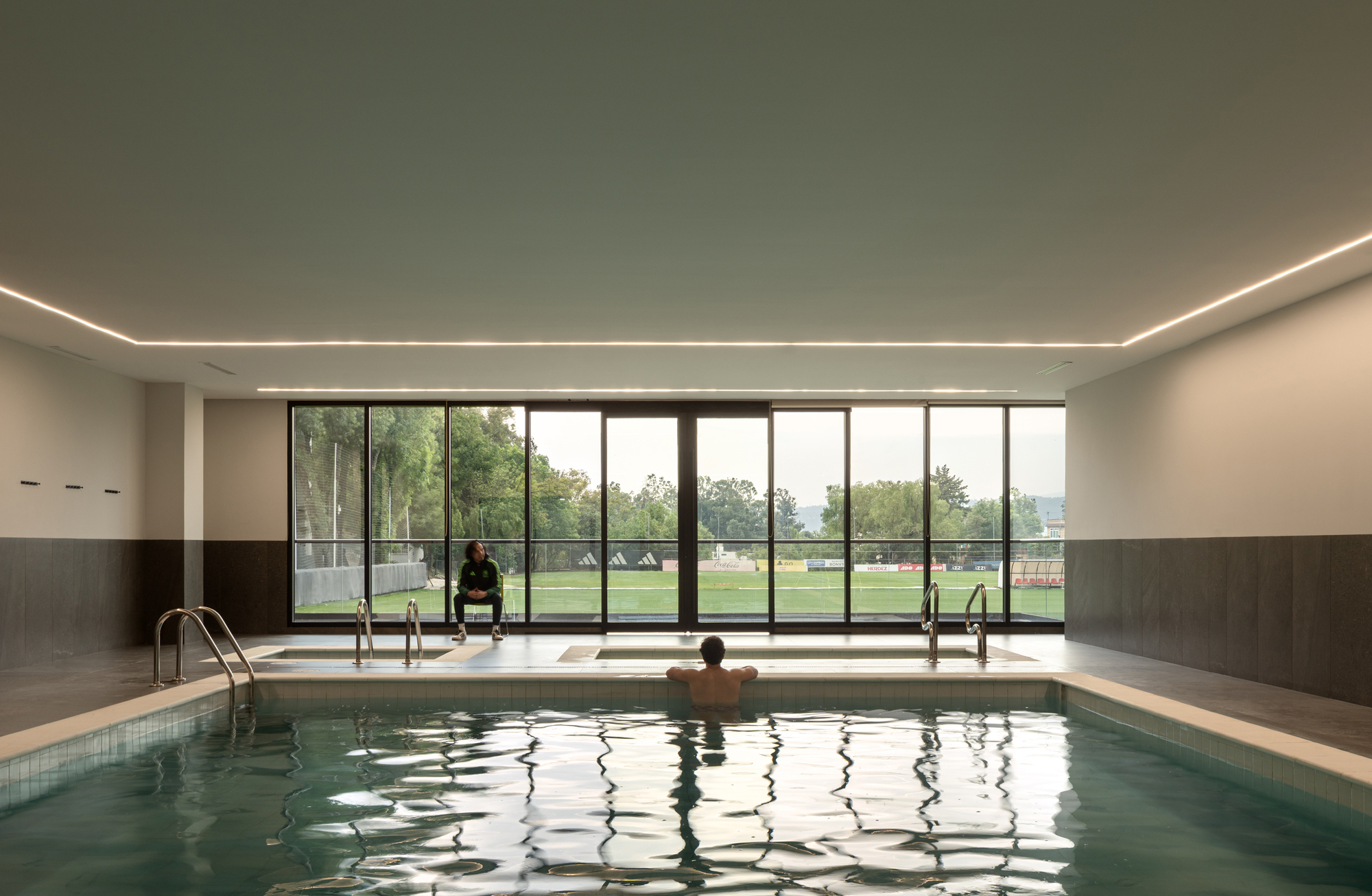 Indoor pool with floor-to-ceiling glazing framing views of the playing field beyond