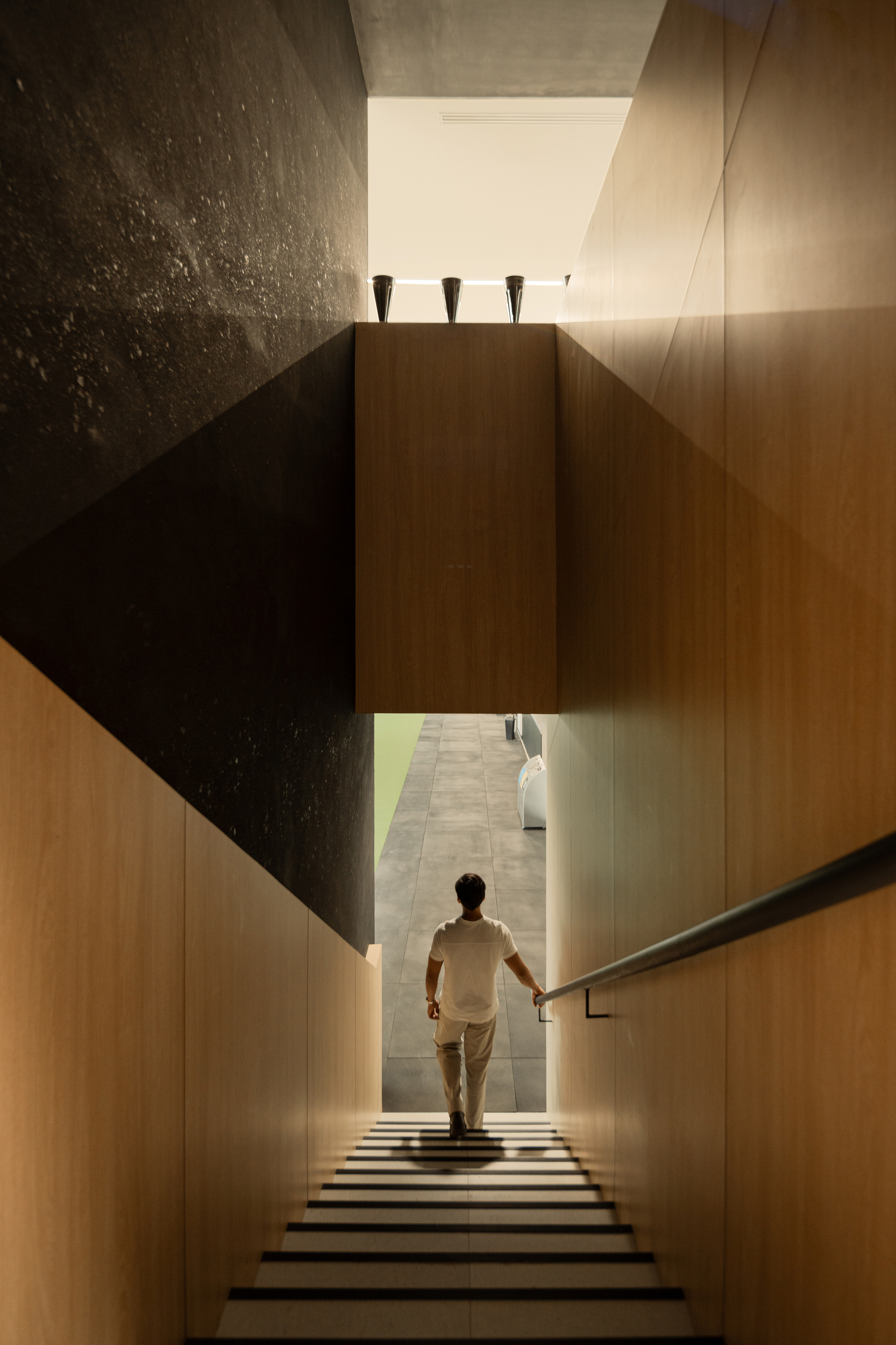 Staircase descending between timber-clad walls with a figure walking toward natural light below