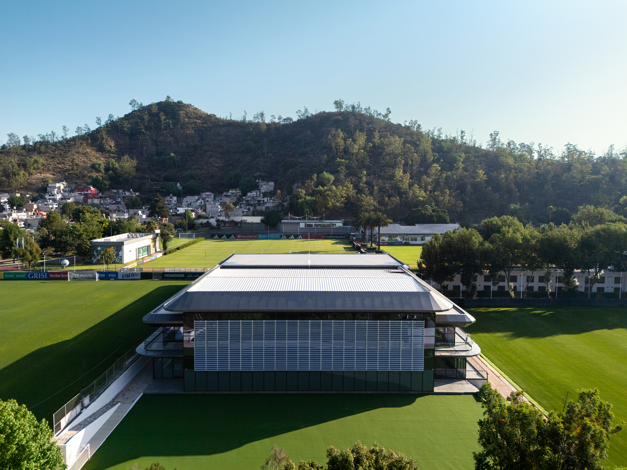 Aerial view of the tiered roof volumes positioned between two playing fields with hills behind