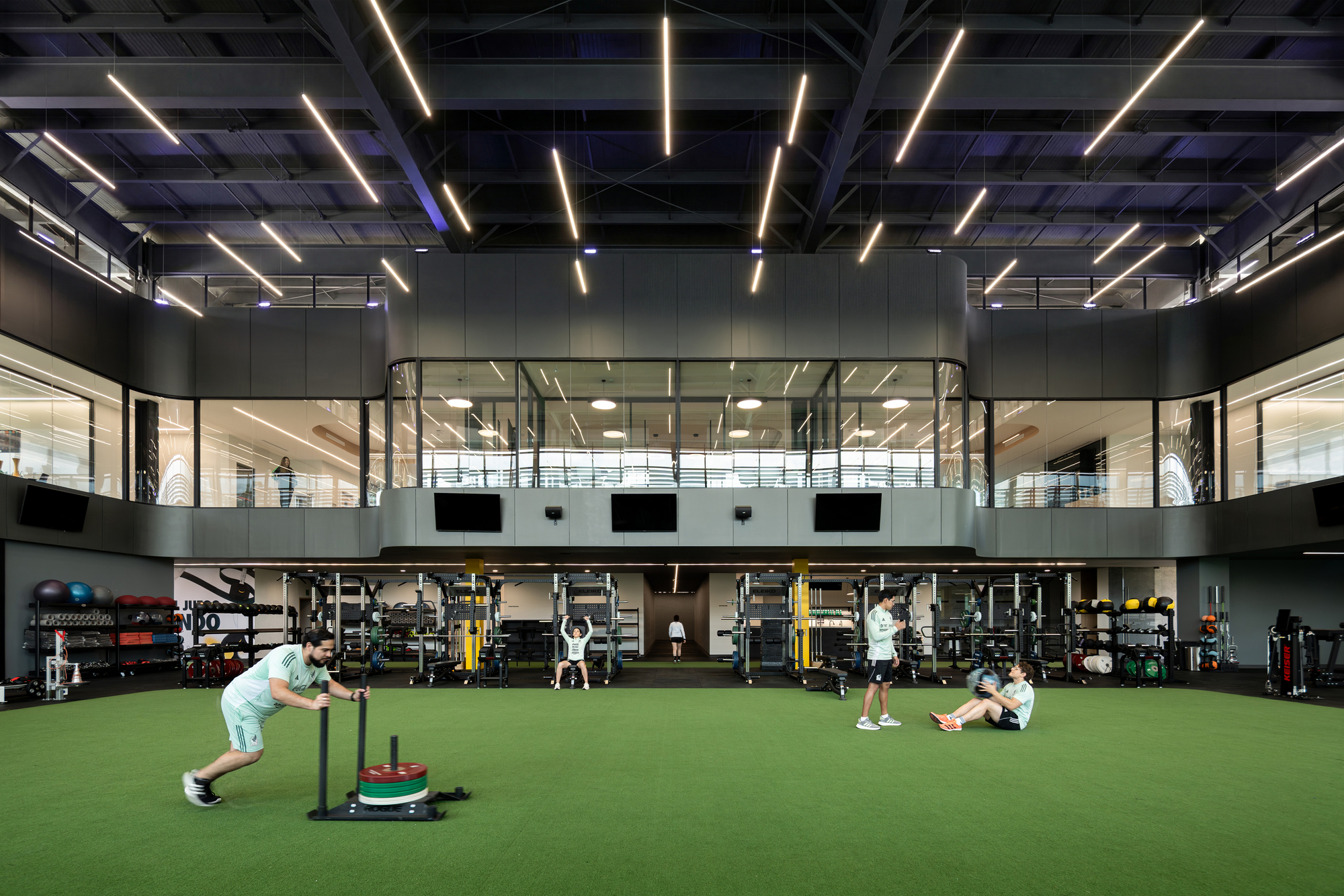 Double-height training facility with artificial turf flooring and suspended linear lighting over the exercise area