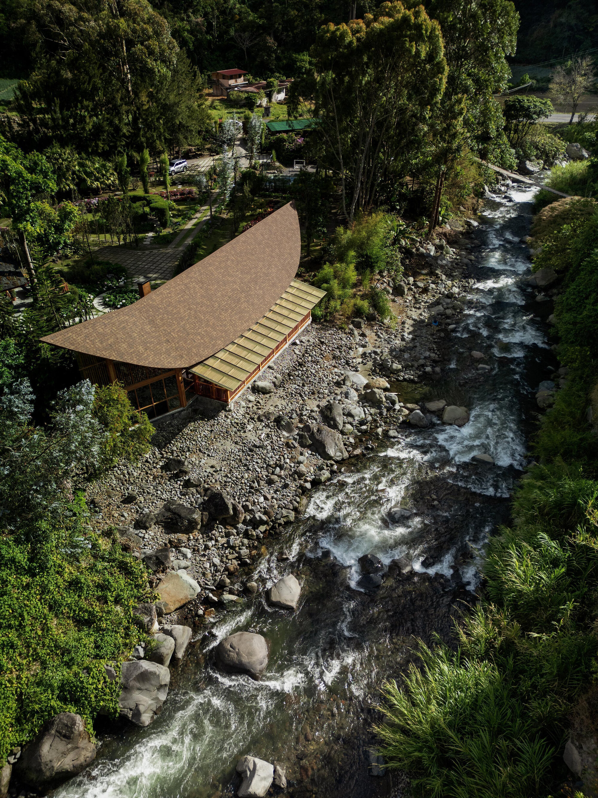 Aerial view of the curved shingled roof cantilevered over a rushing mountain stream with boulders