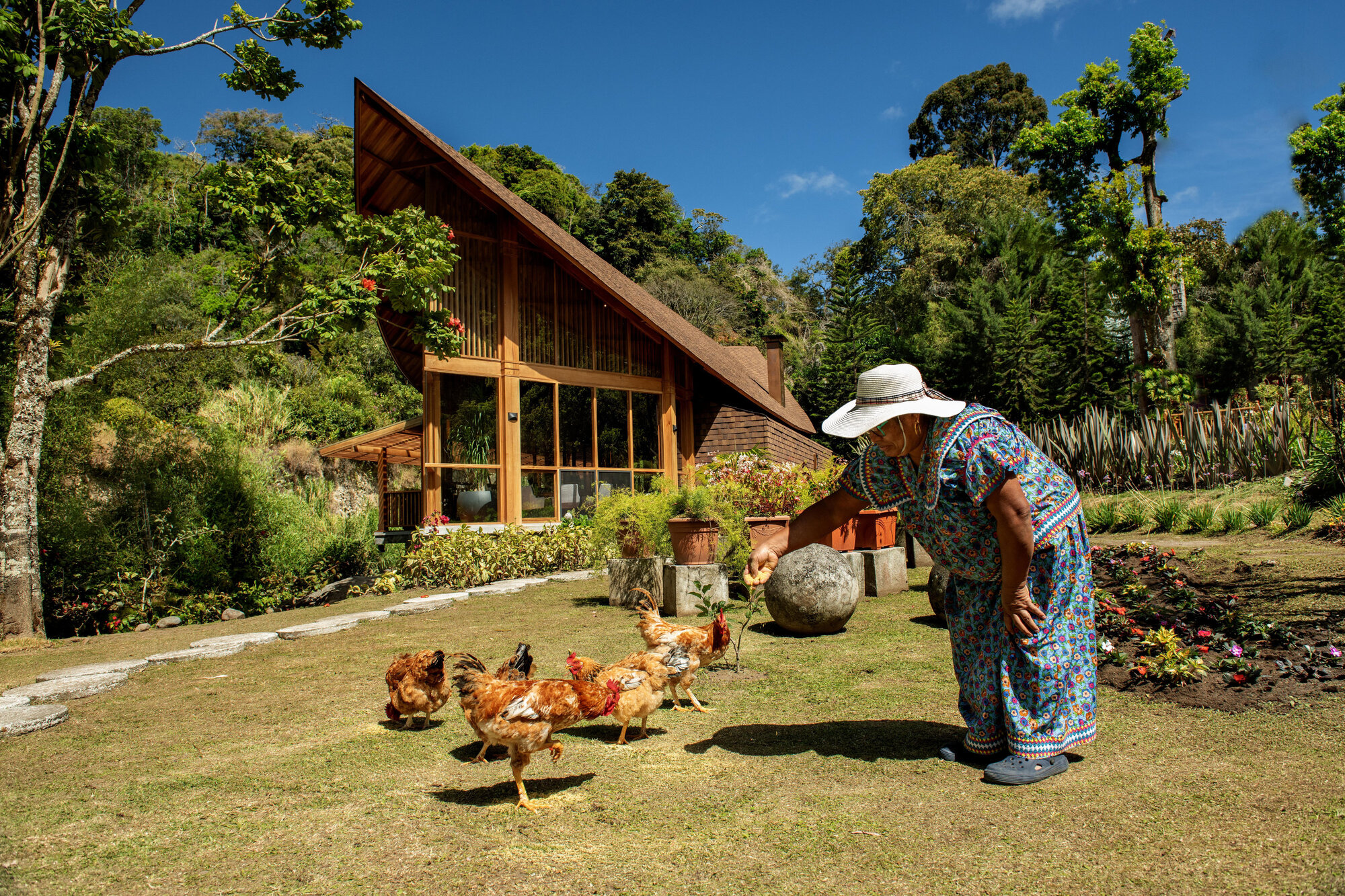 Garden view of the timber-framed facade with a woman feeding chickens on the lawn below