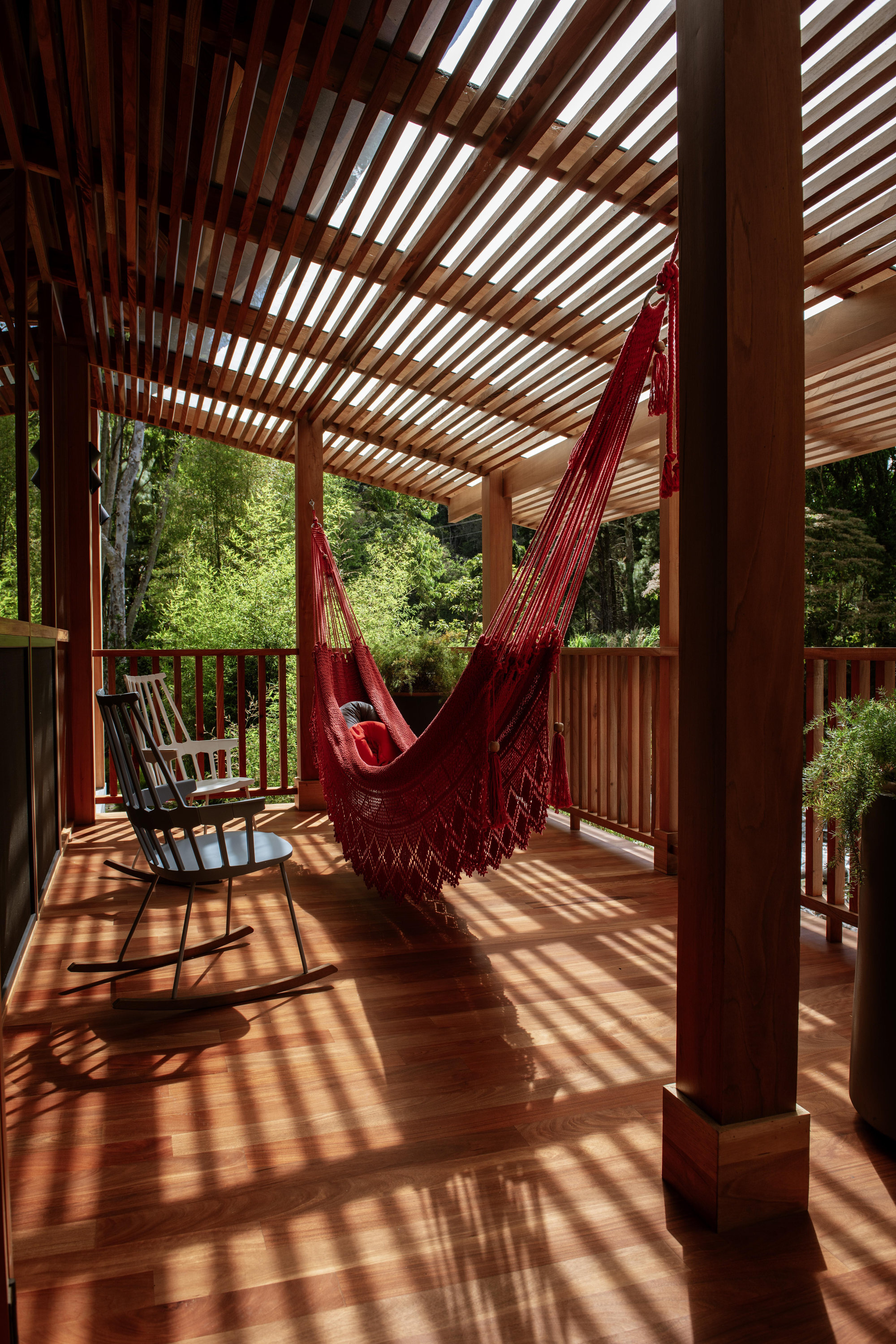 Covered terrace with timber slatted pergola casting dappled shadows on the deck and red hammock