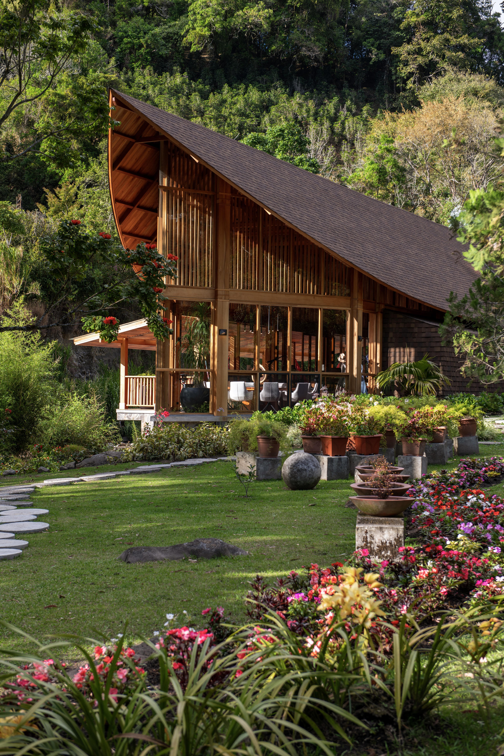 Timber structure with steep sloping roof and vertical slat facade surrounded by flowering garden beds