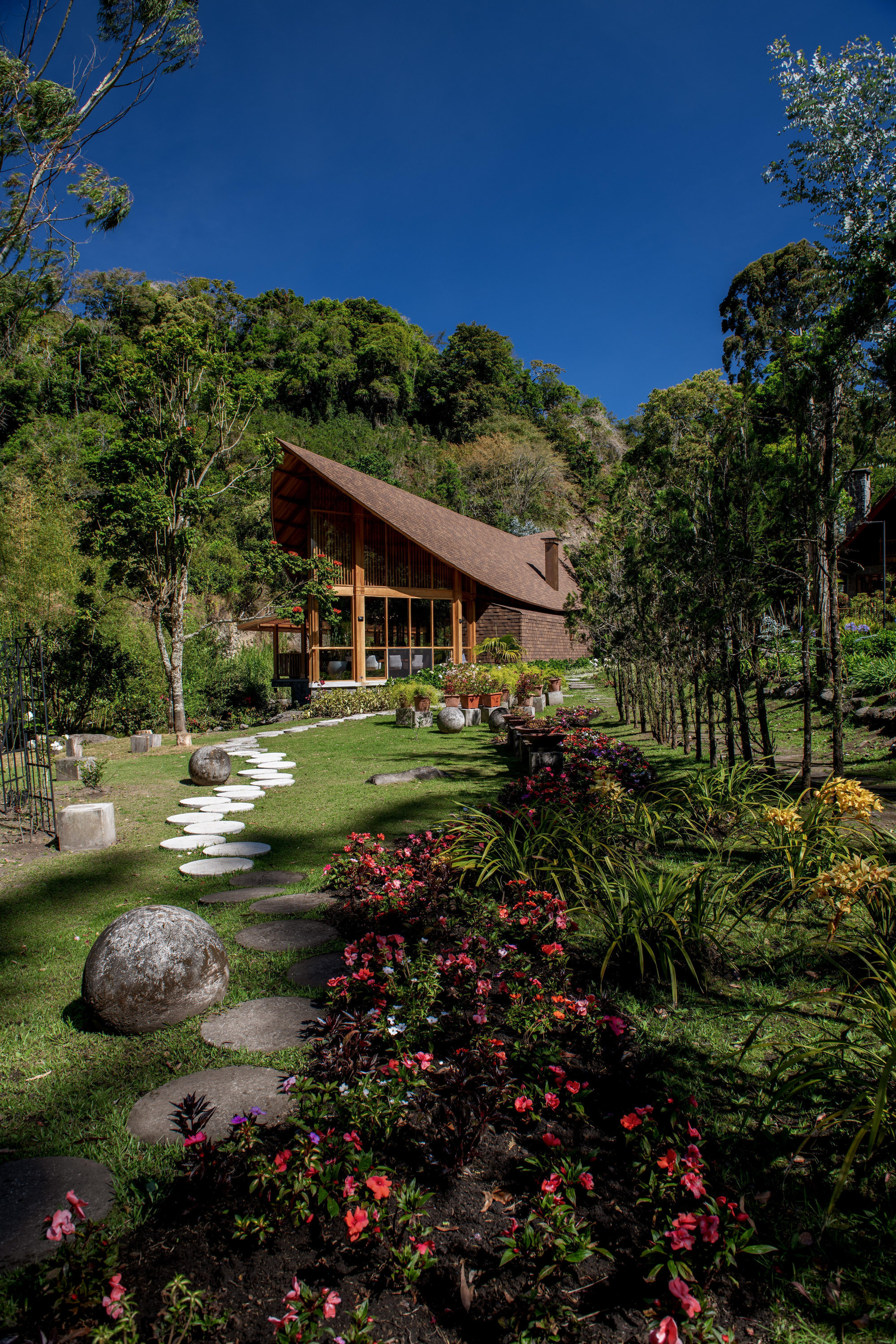Stone stepping path across lawn leading to the timber pavilion framed by trees and flower beds