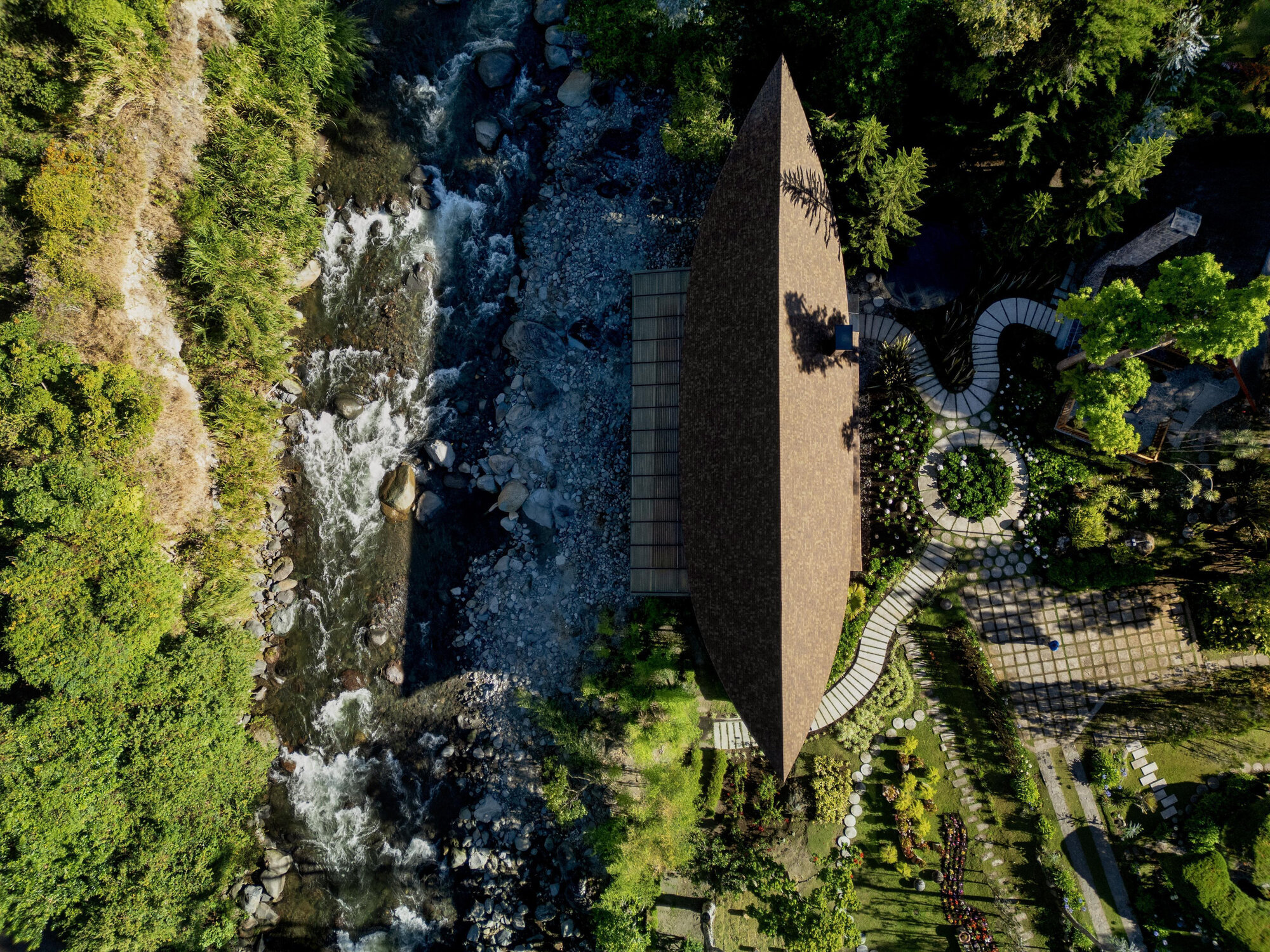 Aerial view of a narrow boat-shaped roof nestled between a rushing river and terraced gardens