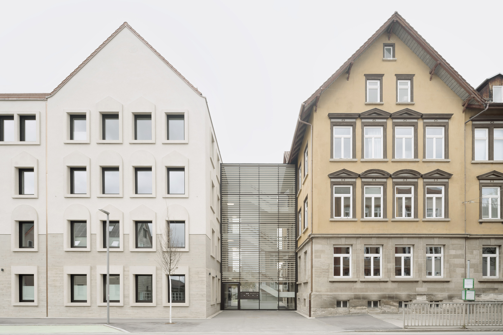 Street view showing a white gabled facade beside a traditional yellow building and a recessed metal screen connector