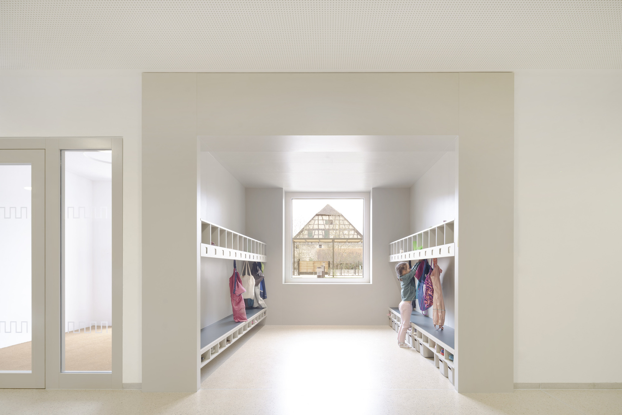 White hallway with coat hooks and benches framing a centered window view of a timber-framed barn
