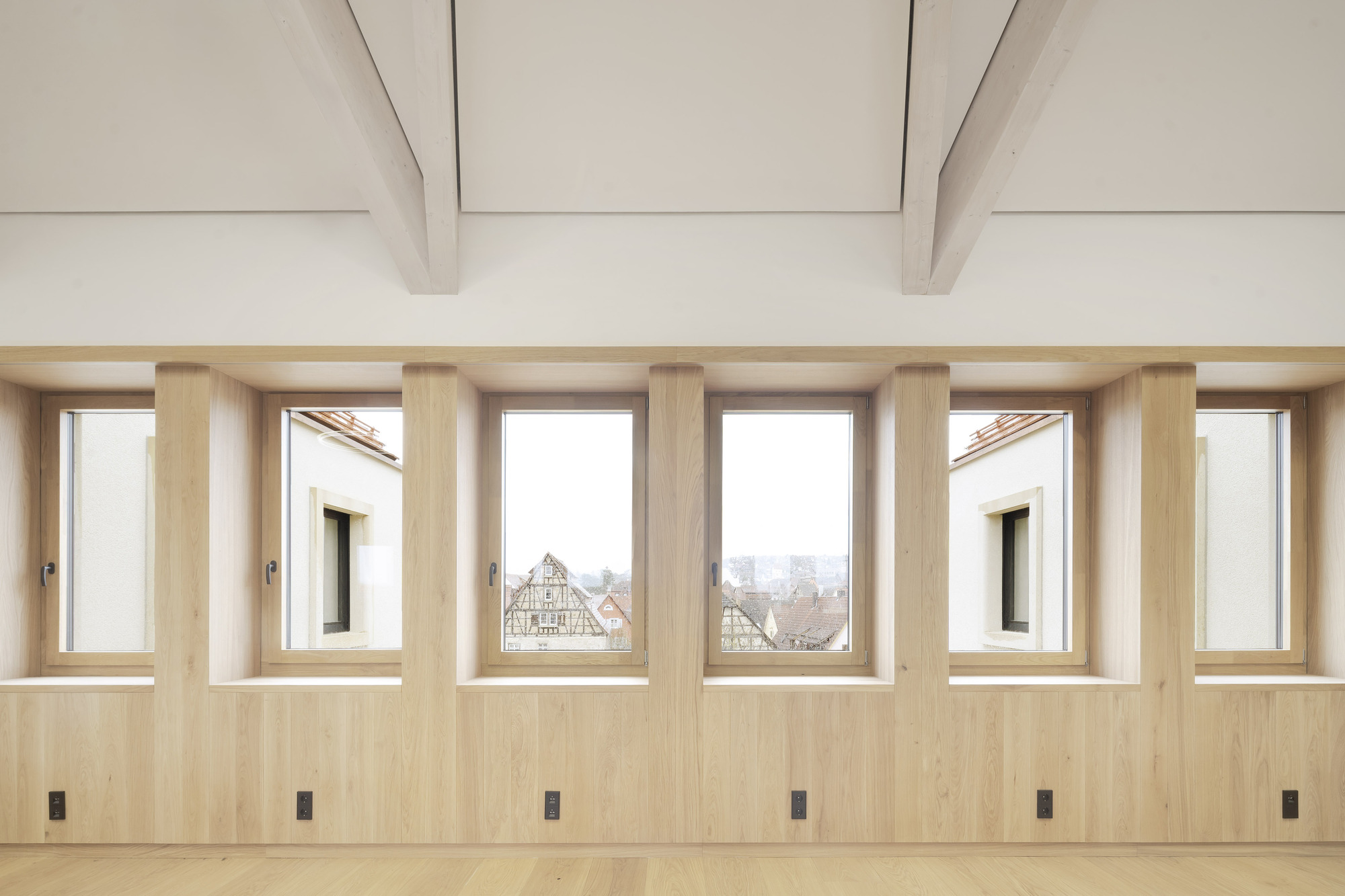 Six tall windows framed in light wood with views of traditional rooftops and exposed ceiling beams