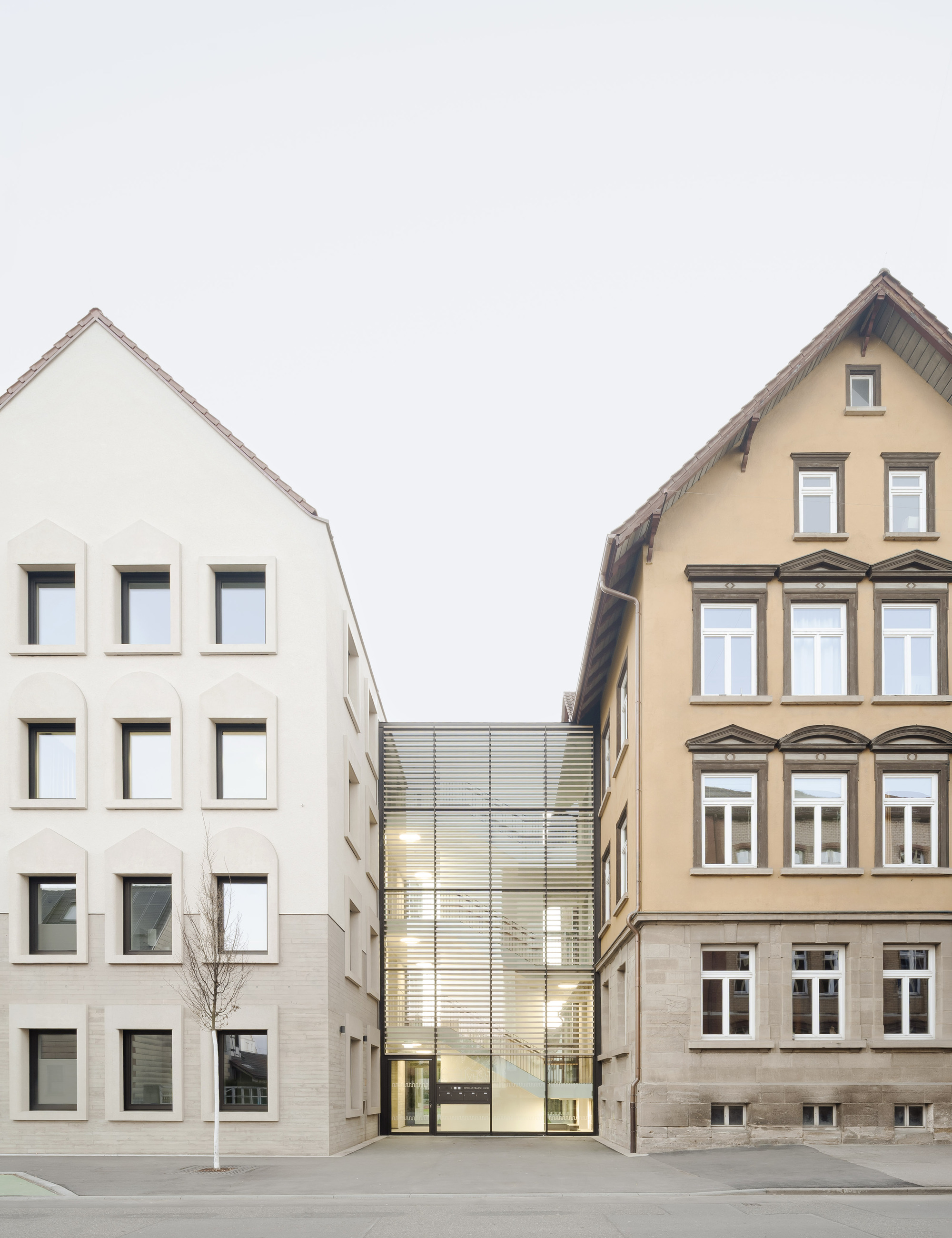 Street view showing a metal-clad connector volume between a white plastered building and a historic facade