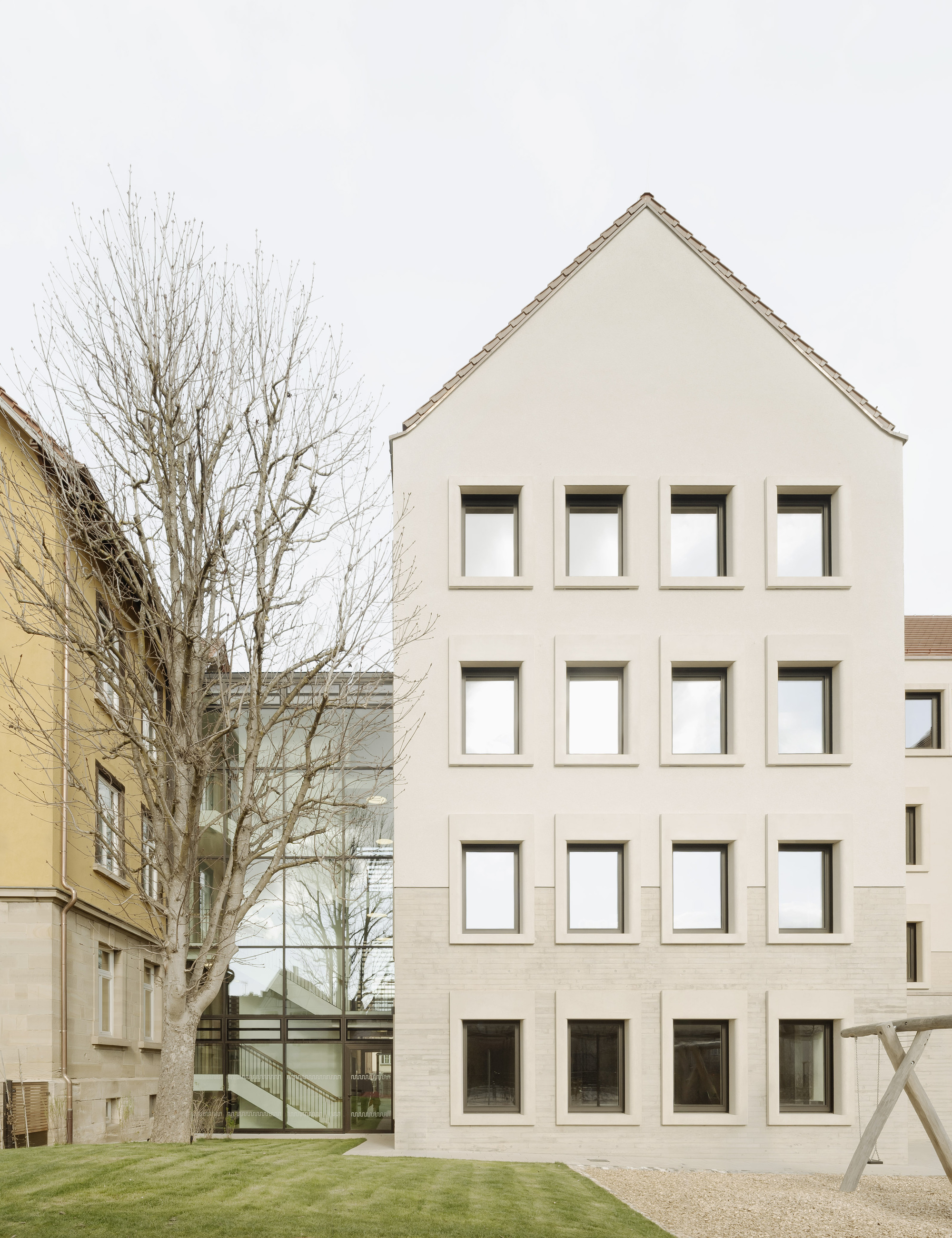 Front facade with gabled roof and grid of square windows beside a bare winter tree