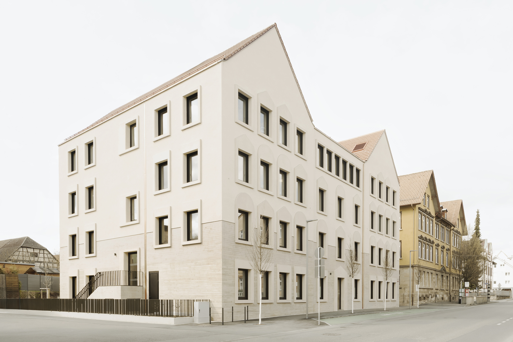 Street corner view of the pale plastered volumes with small vertical windows under cloudy sky