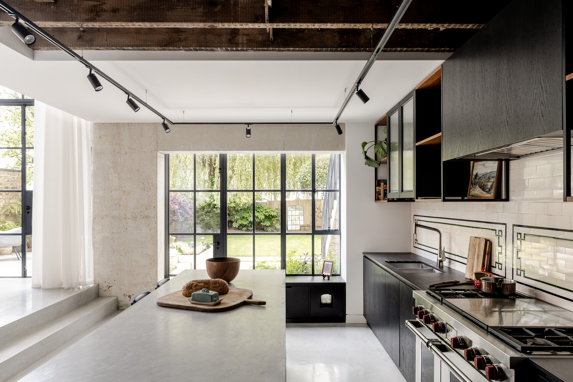 Kitchen with dark cabinetry and exposed timber ceiling looking toward steel-framed window and garden